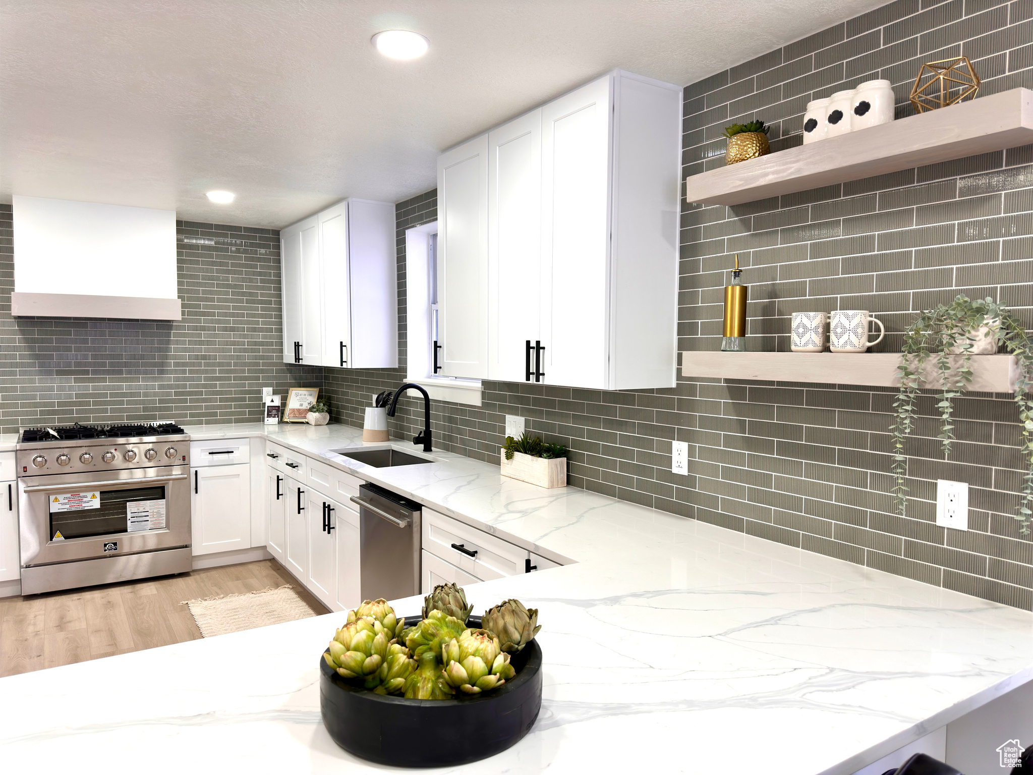 Kitchen with sink, wall chimney exhaust hood, light stone counters, white cabinetry, and stainless steel appliances