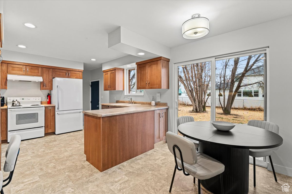 Kitchen featuring kitchen peninsula, white appliances, sink, and a breakfast bar