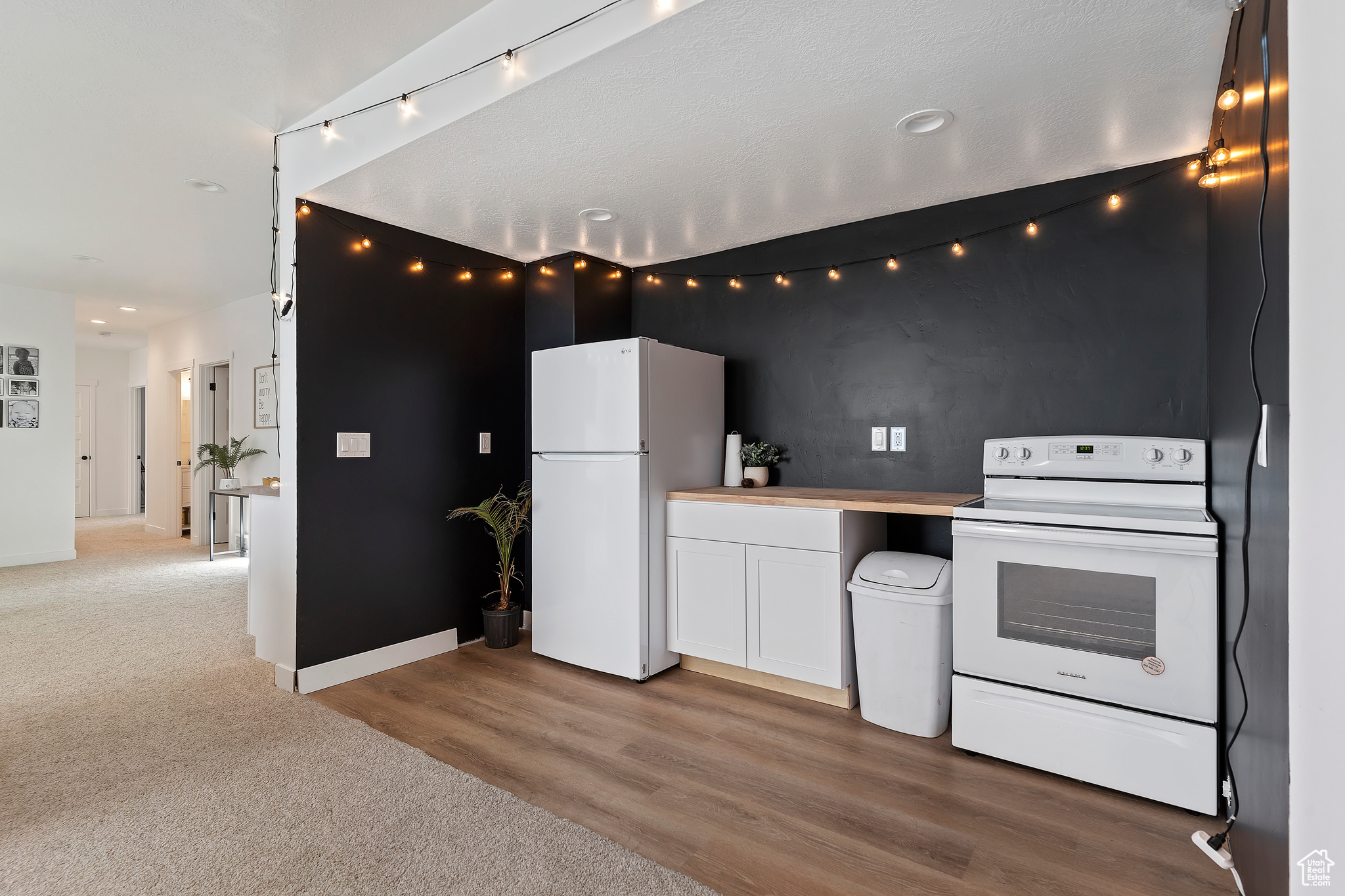 Kitchen featuring carpet, white appliances, and white cabinetry