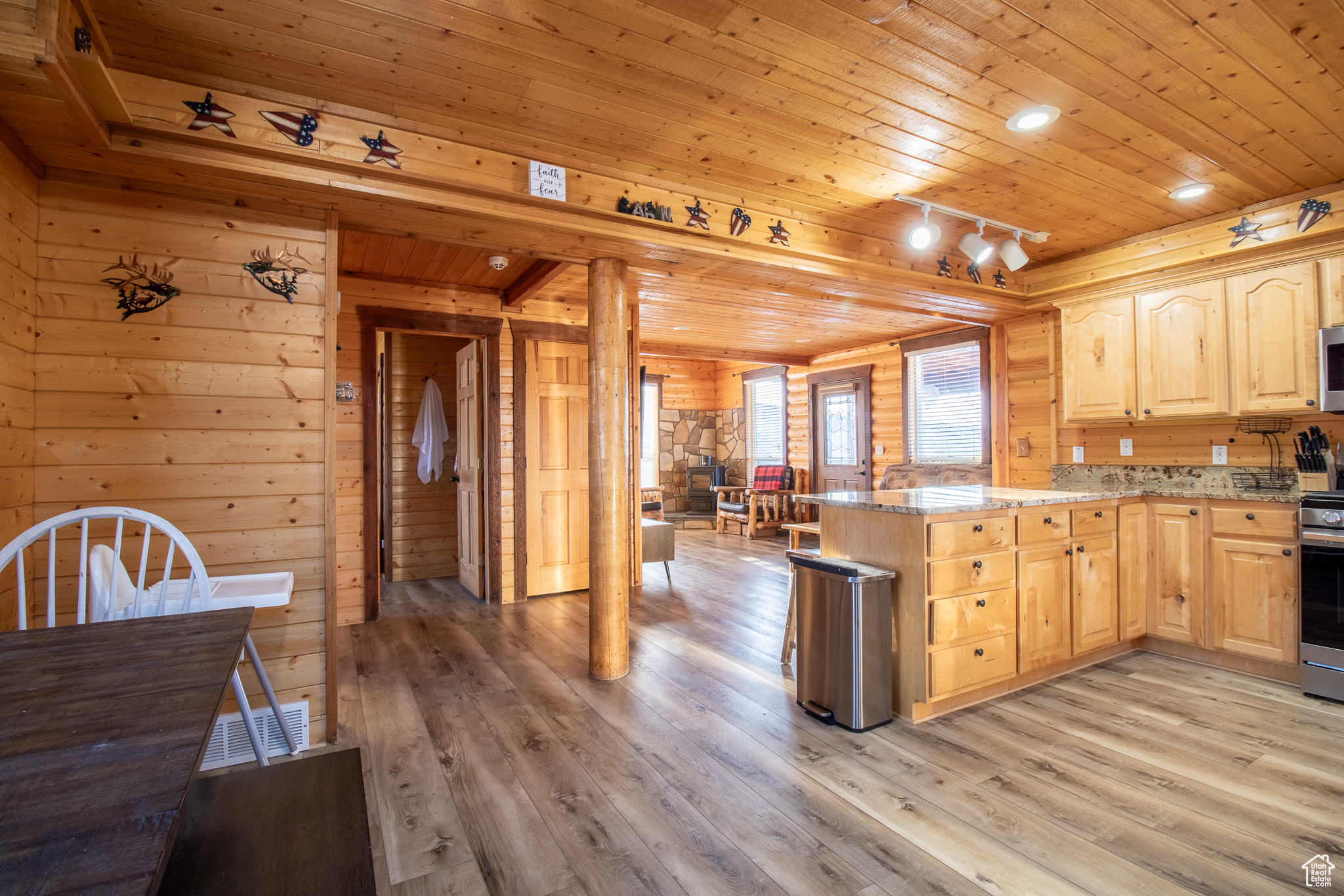 Kitchen with light stone countertops, light brown cabinets, wooden ceiling, and wood walls