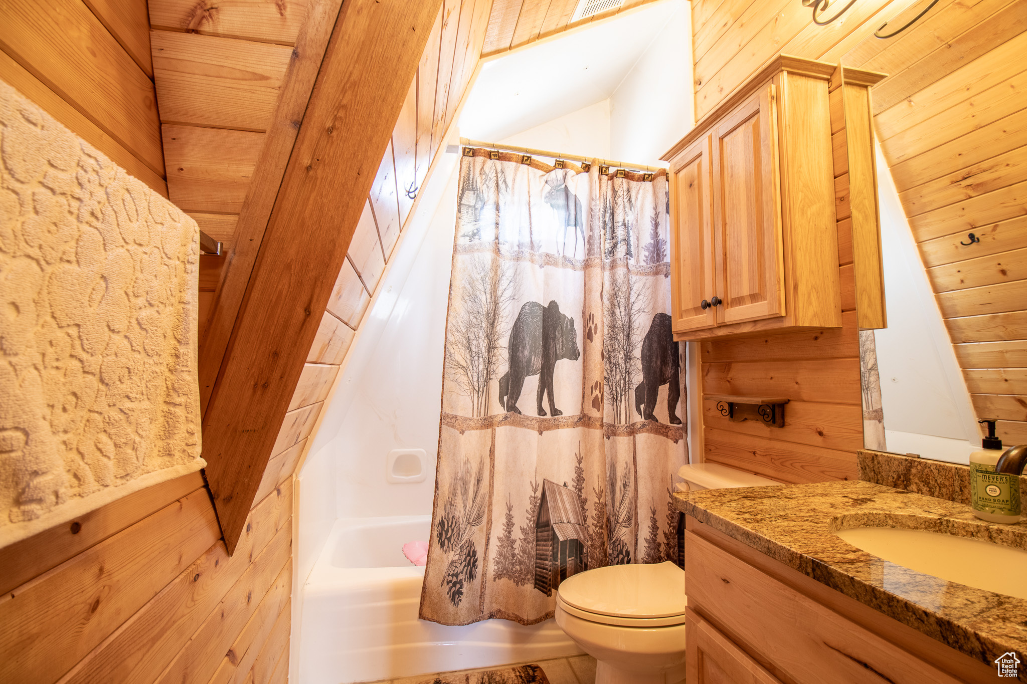 Full bathroom with wood ceiling, vanity, shower / bath combo with shower curtain, wooden walls, and toilet