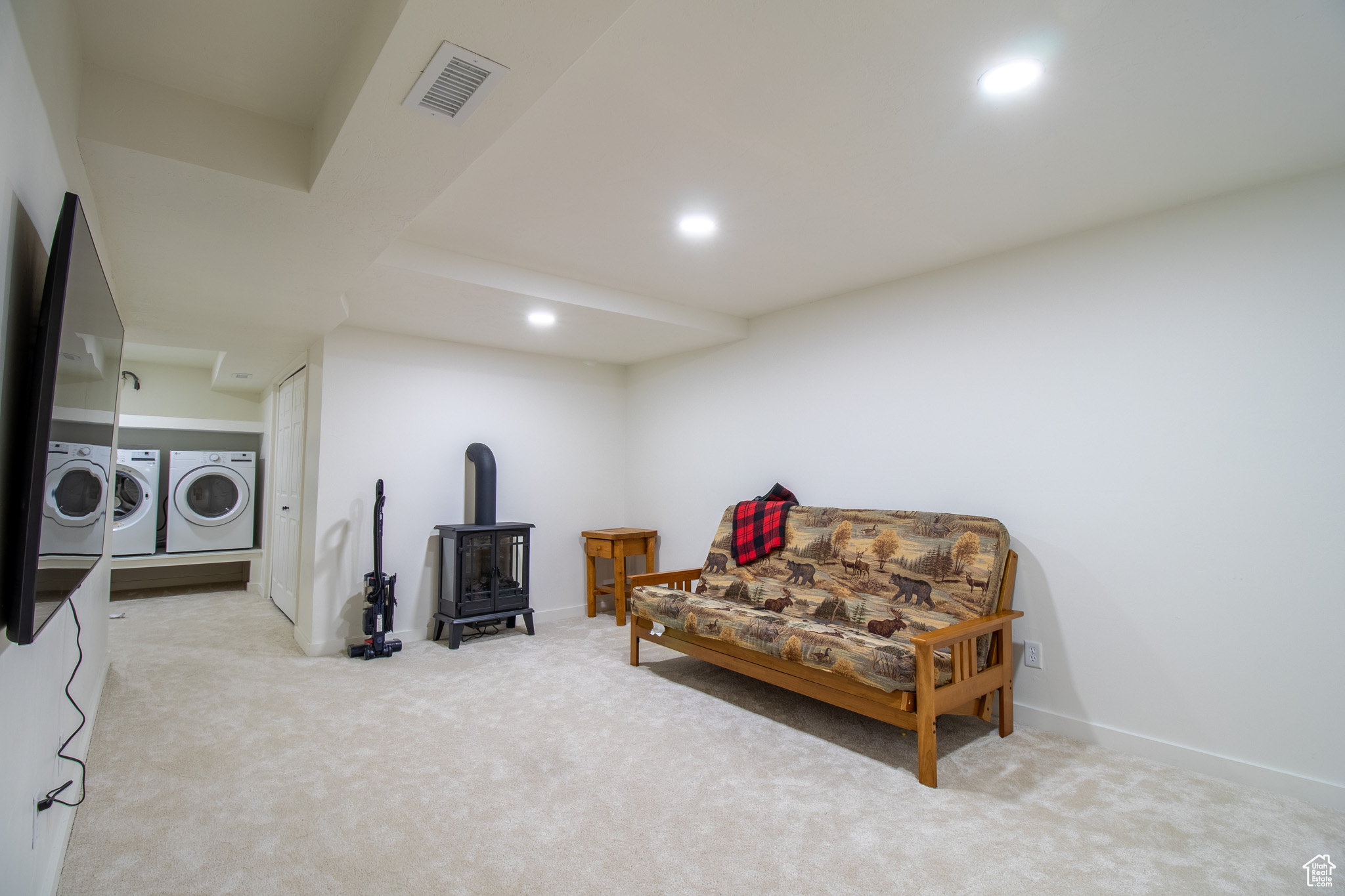 Sitting room with light colored carpet, a wood stove, and washer and clothes dryer