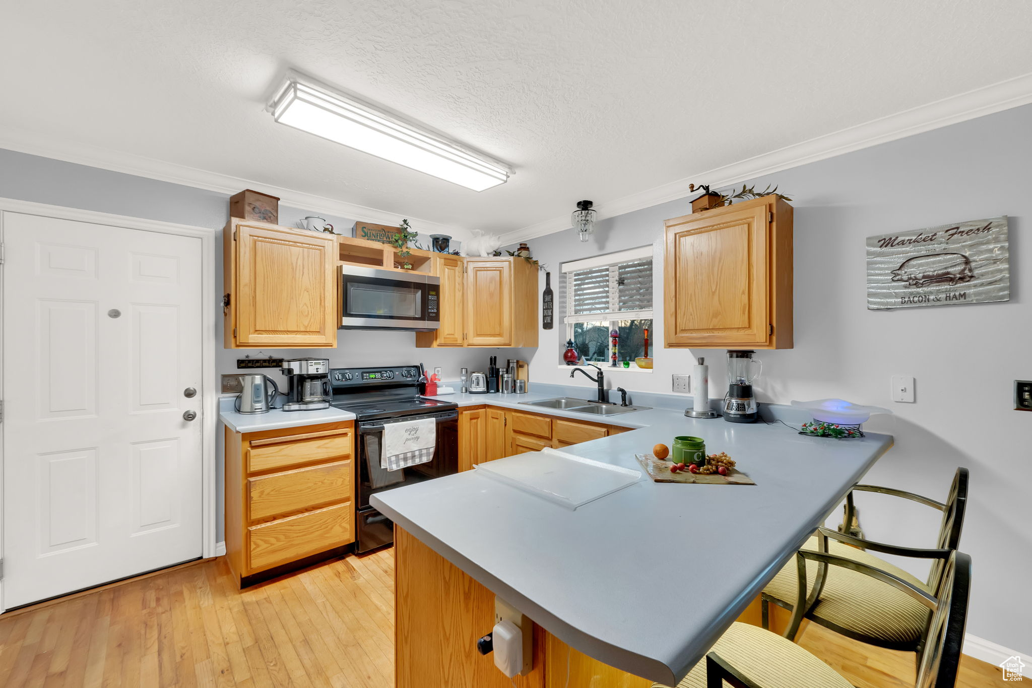 Kitchen with a kitchen breakfast bar, black range with electric stovetop, sink, crown molding, and kitchen peninsula