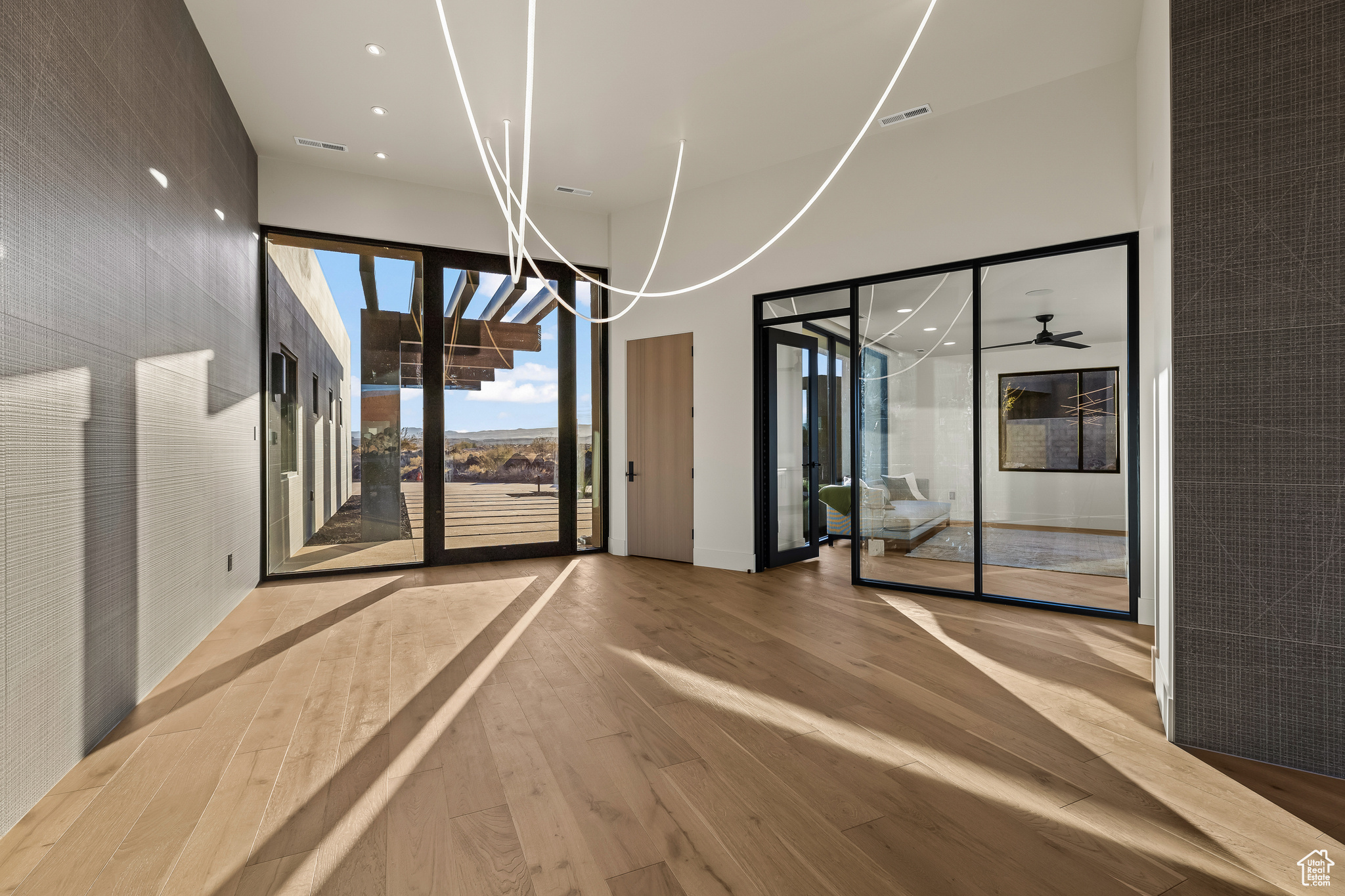 Empty room with a towering ceiling, light hardwood / wood-style floors, and ceiling fan with notable chandelier