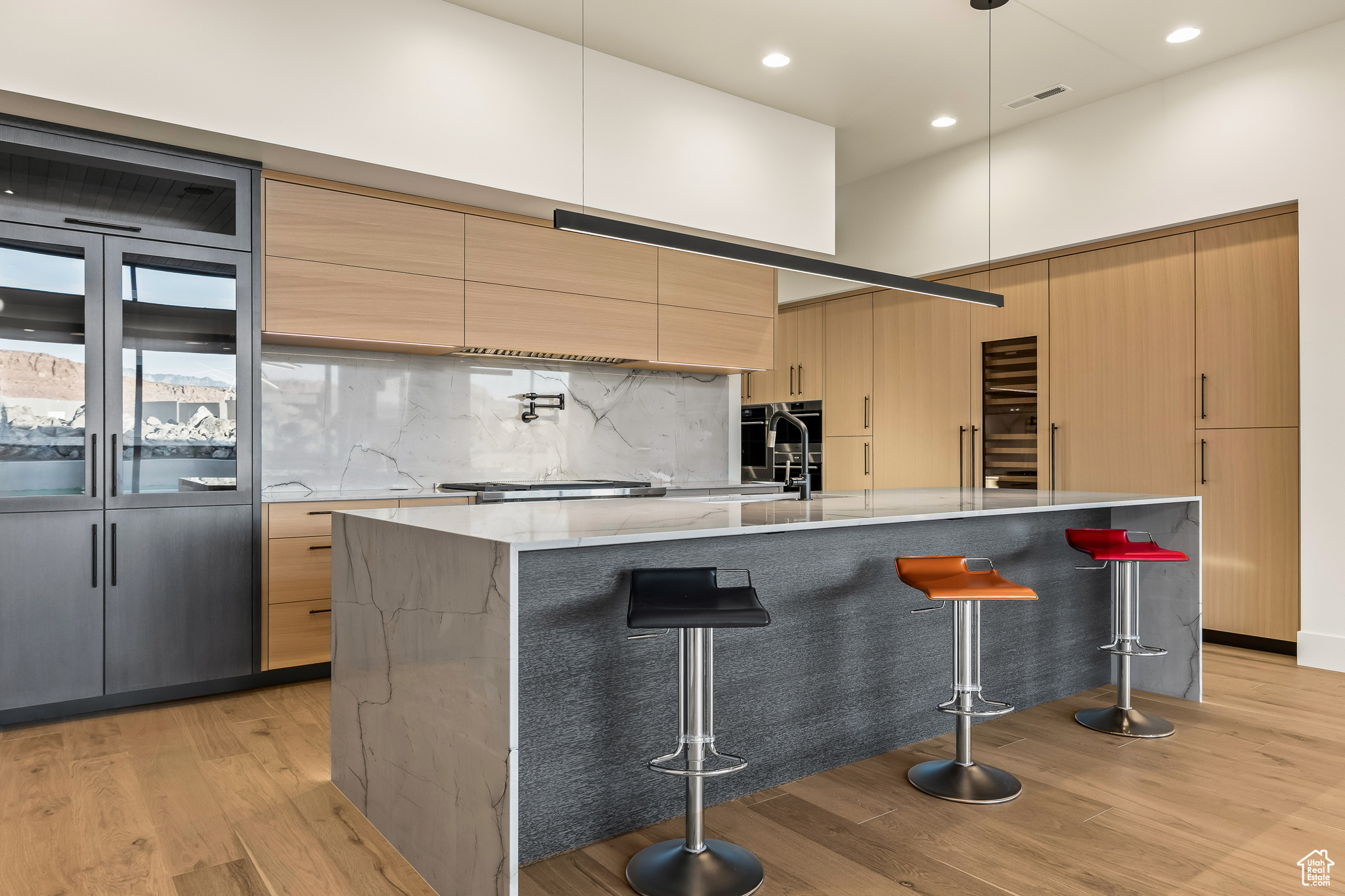 Kitchen with a large island, light hardwood / wood-style flooring, backsplash, decorative light fixtures, and a kitchen bar