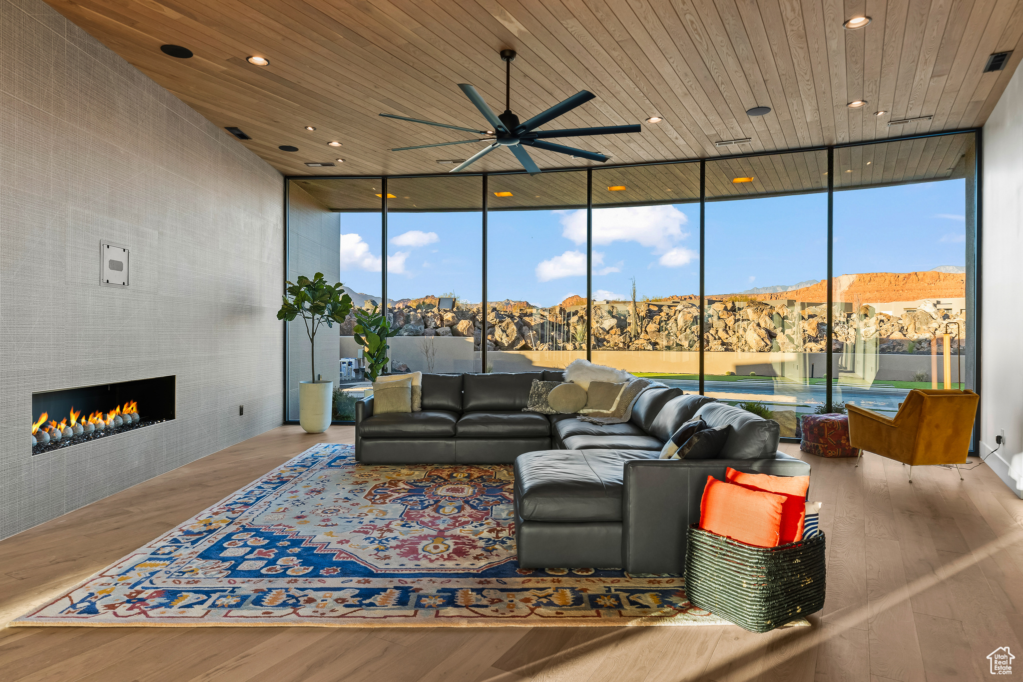 Living room with floor to ceiling windows, wood ceiling, a tiled fireplace, and light wood-type flooring