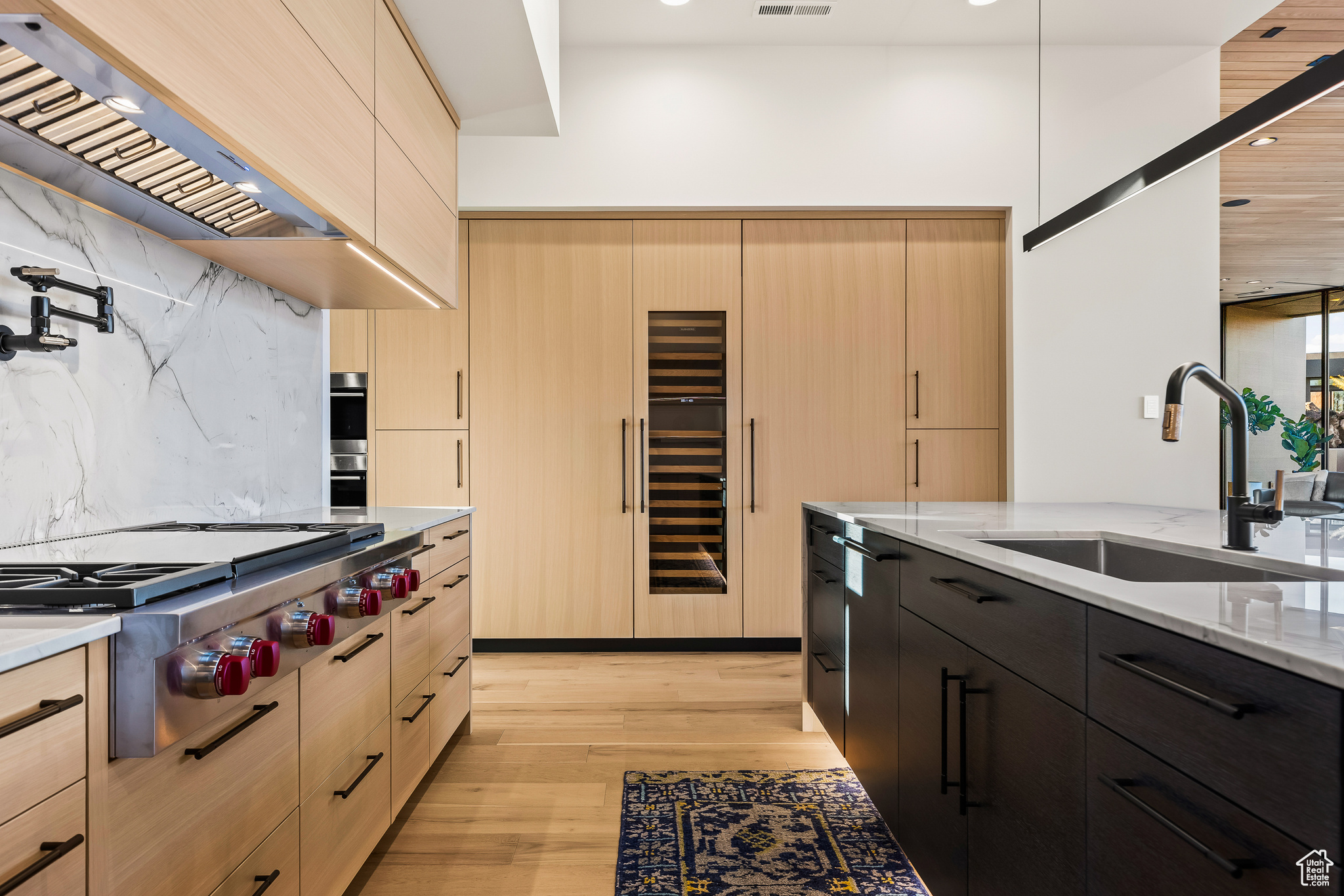 Kitchen with premium range hood, light stone counters, sink, light brown cabinets, and stainless steel gas stovetop