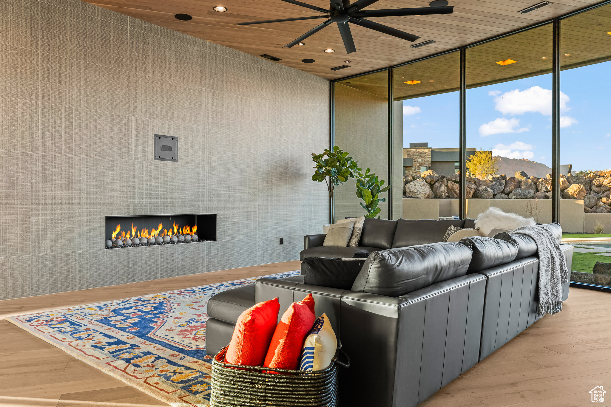 Living room with light wood-type flooring, floor to ceiling windows, ceiling fan, wooden ceiling, and a tiled fireplace