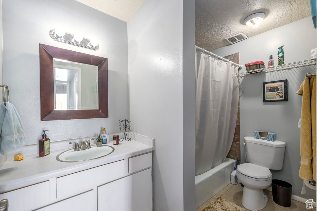 Full bathroom with tile patterned flooring, a textured ceiling, toilet, shower / tub combo with curtain, and vanity