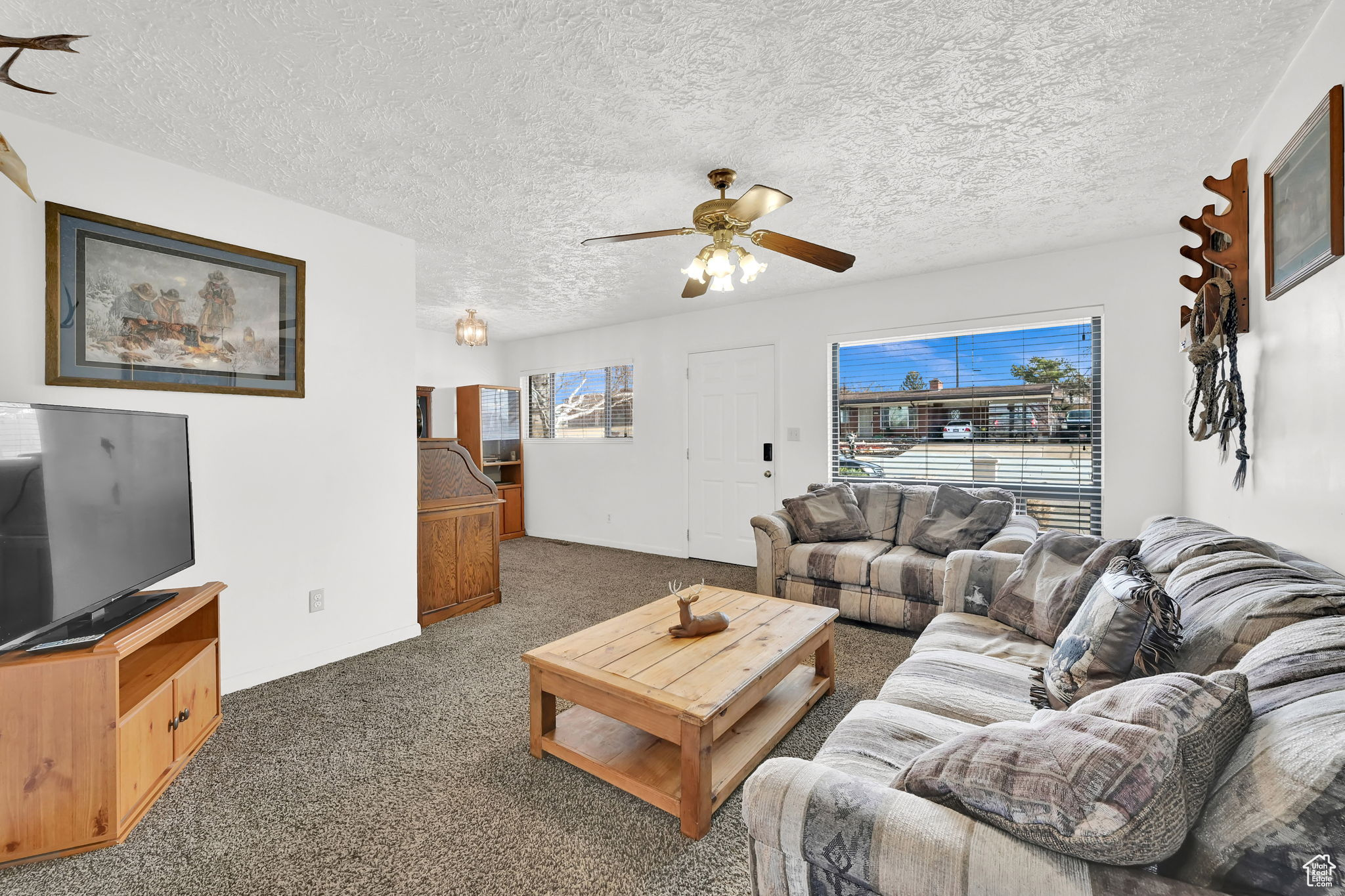 Living room featuring a textured ceiling, dark carpet, and ceiling fan