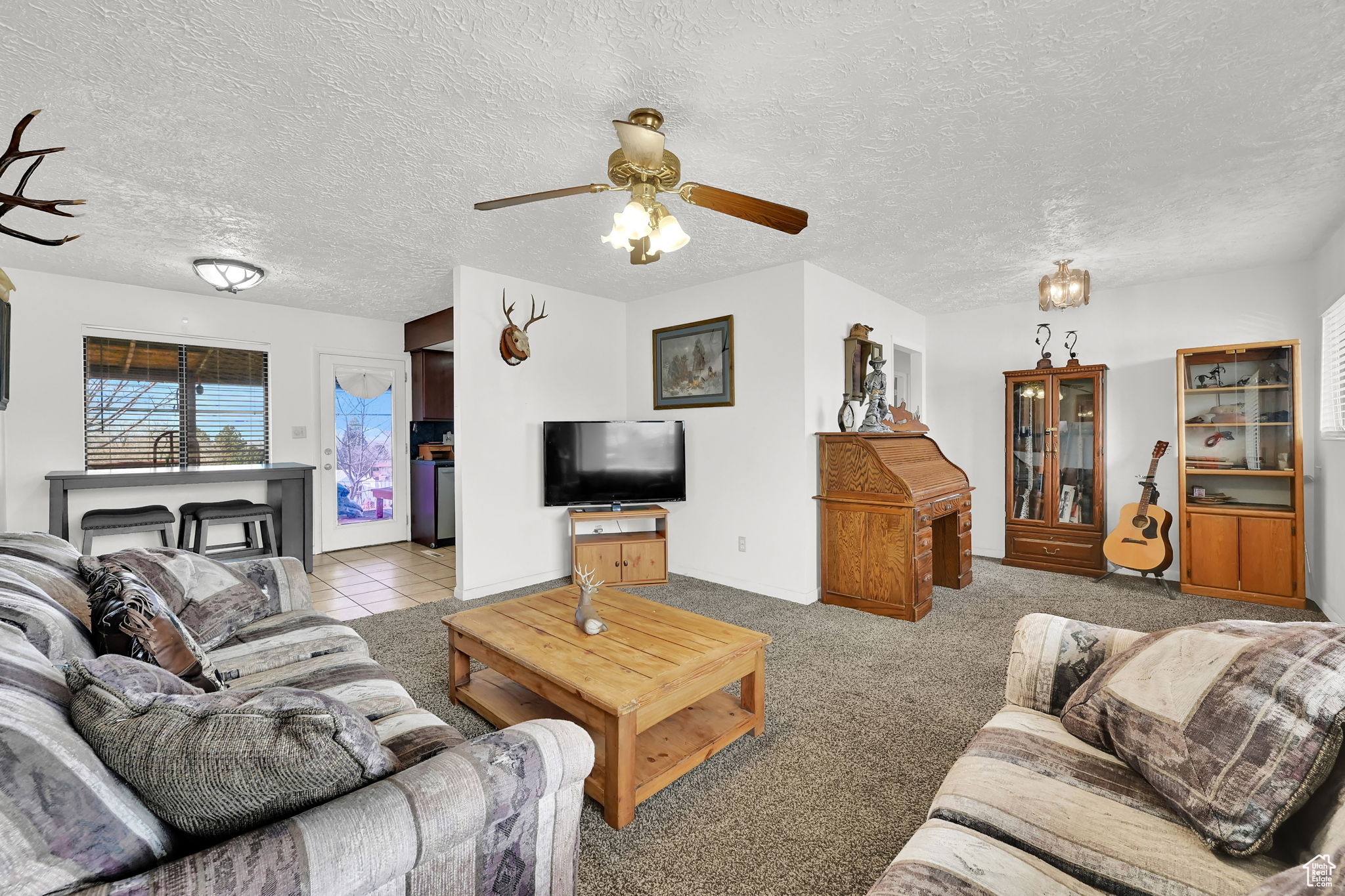 Carpeted living room featuring ceiling fan and a textured ceiling