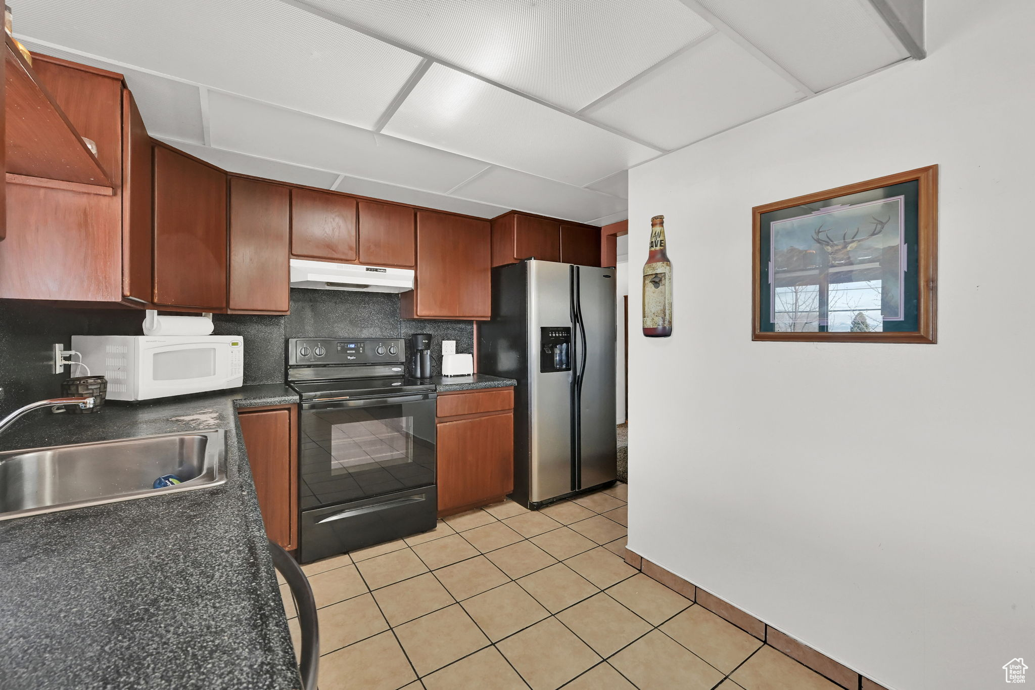 Kitchen with electric range, sink, stainless steel fridge with ice dispenser, backsplash, and light tile patterned floors