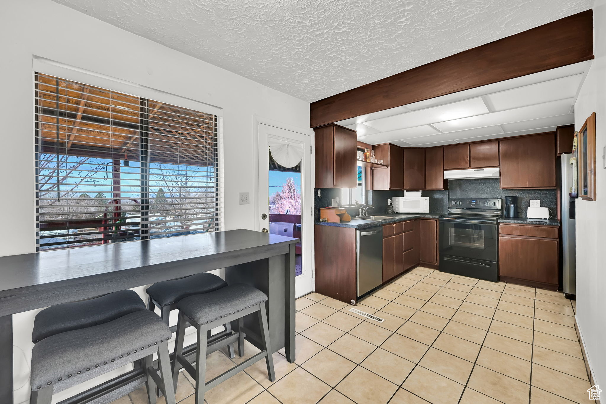 Kitchen with backsplash, sink, a textured ceiling, light tile patterned flooring, and stainless steel appliances