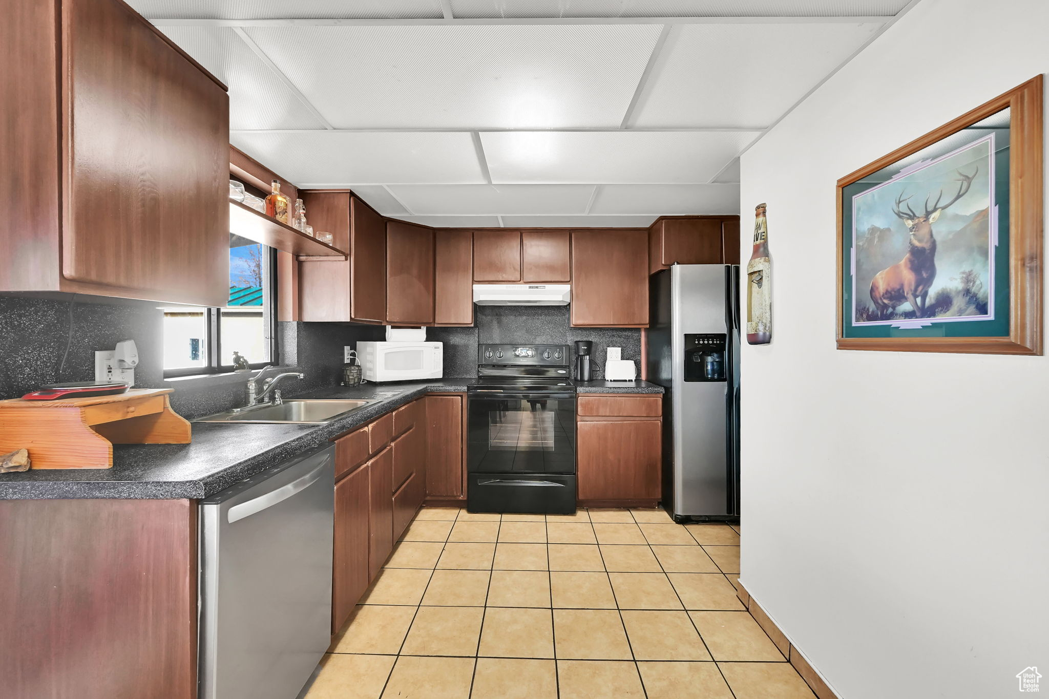 Kitchen with light tile patterned floors, backsplash, stainless steel appliances, and sink