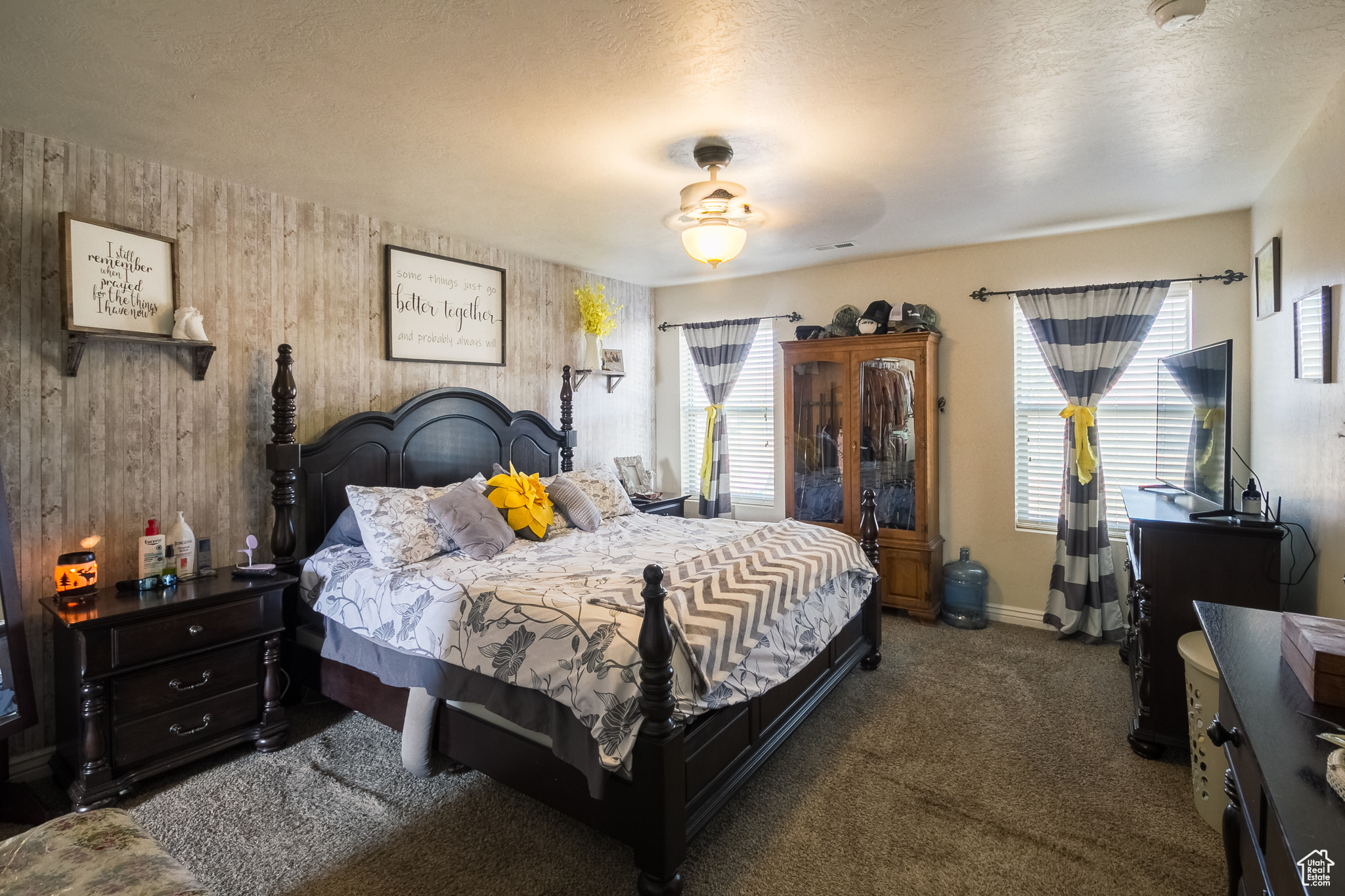 Carpeted master bedroom with wooden walls, ceiling fan, and a textured ceiling