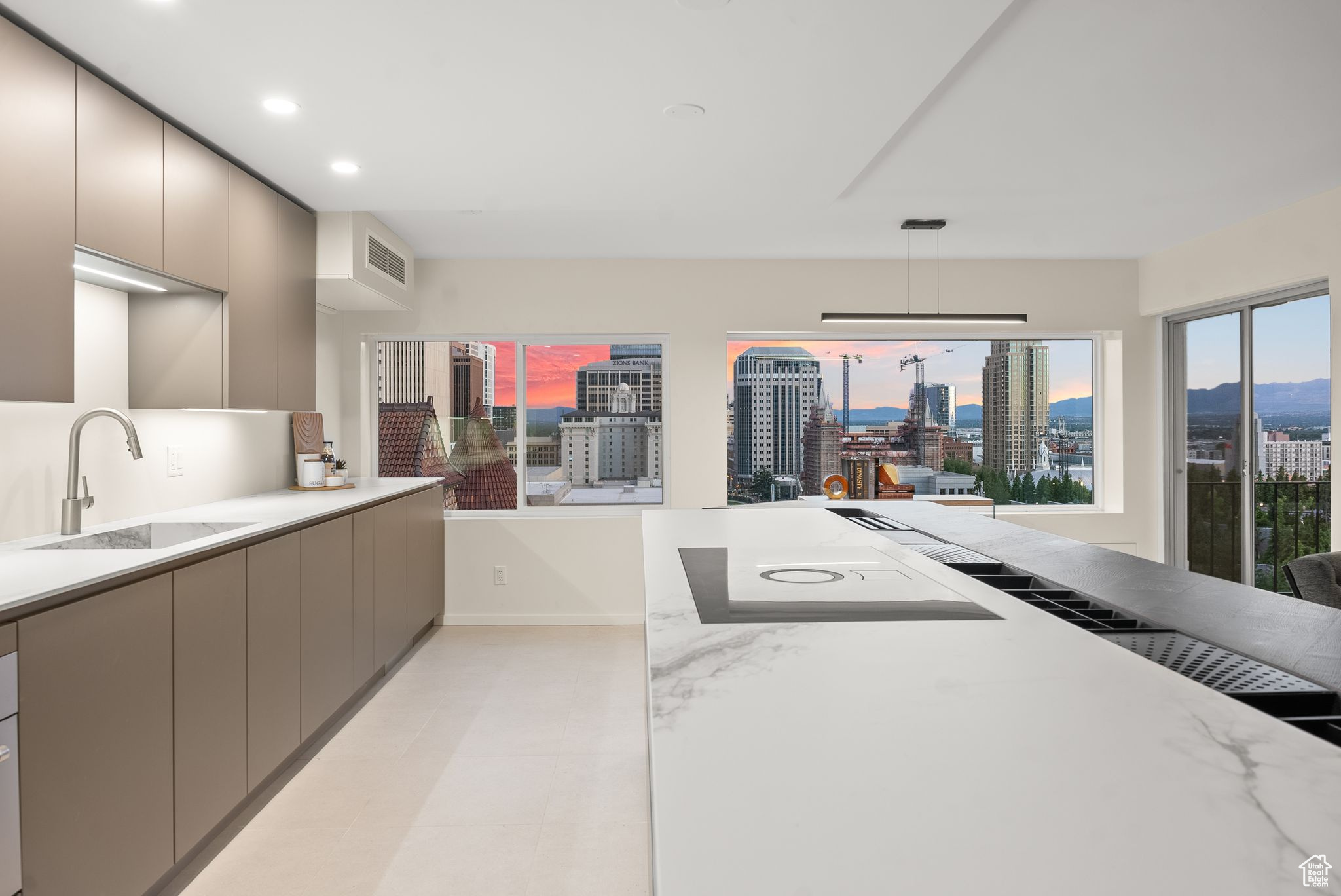 Kitchen featuring light stone countertops, gray cabinets, hanging light fixtures, and sink