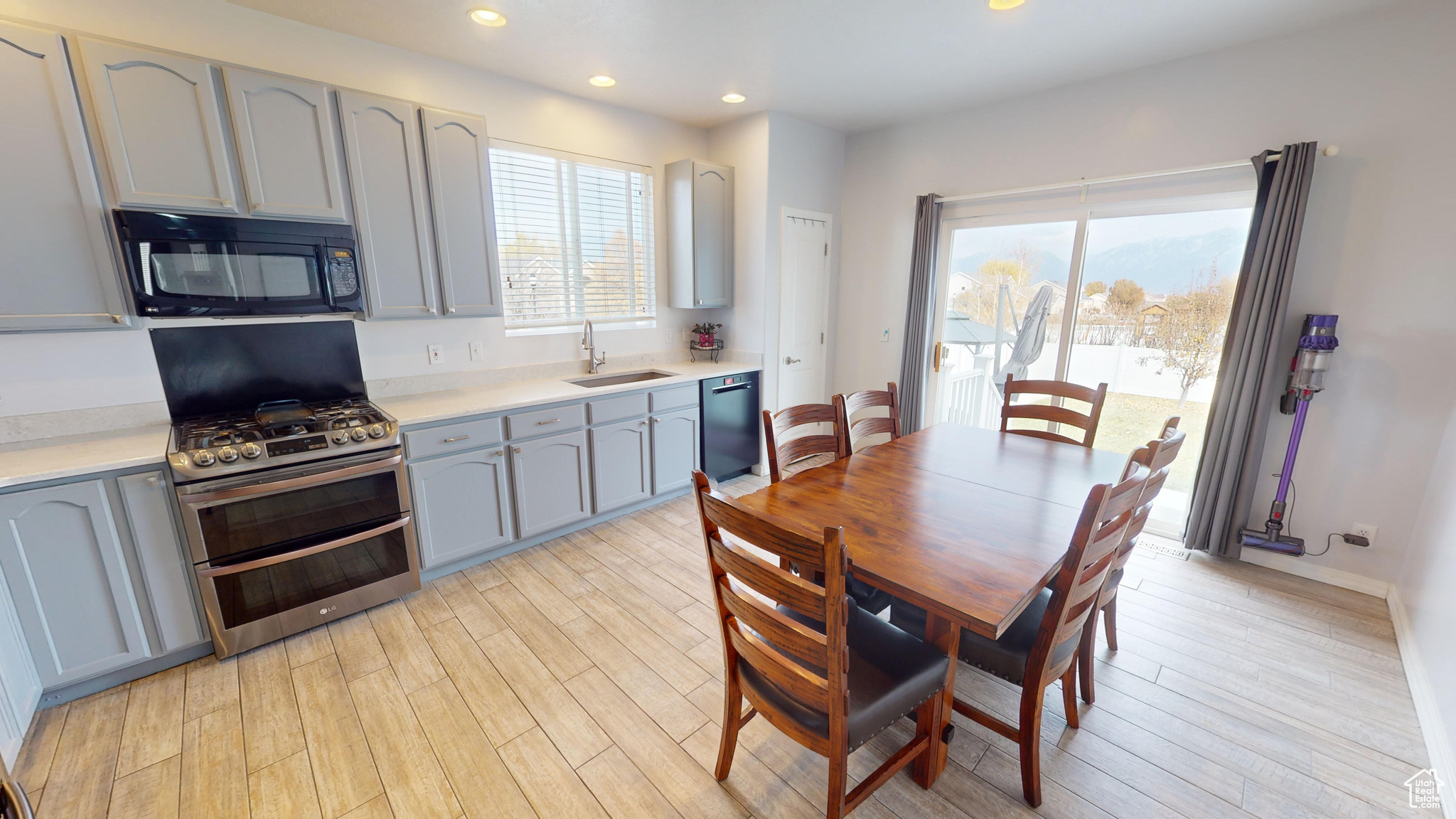 Kitchen with black appliances, light hardwood / wood-style floors, gray cabinetry, and sink