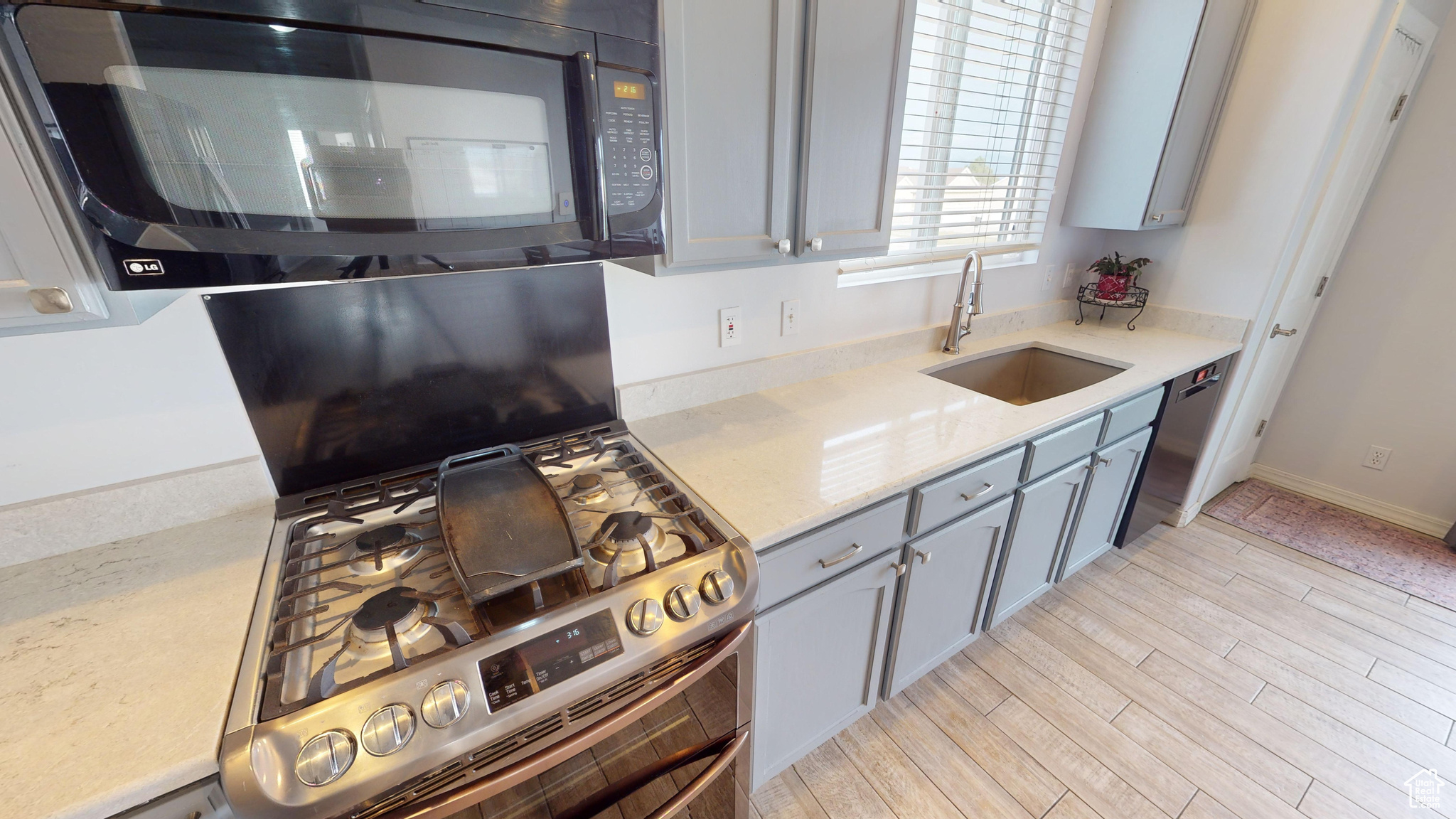 Kitchen with sink, light stone counters, gray cabinets, appliances with stainless steel finishes, and light wood-type flooring