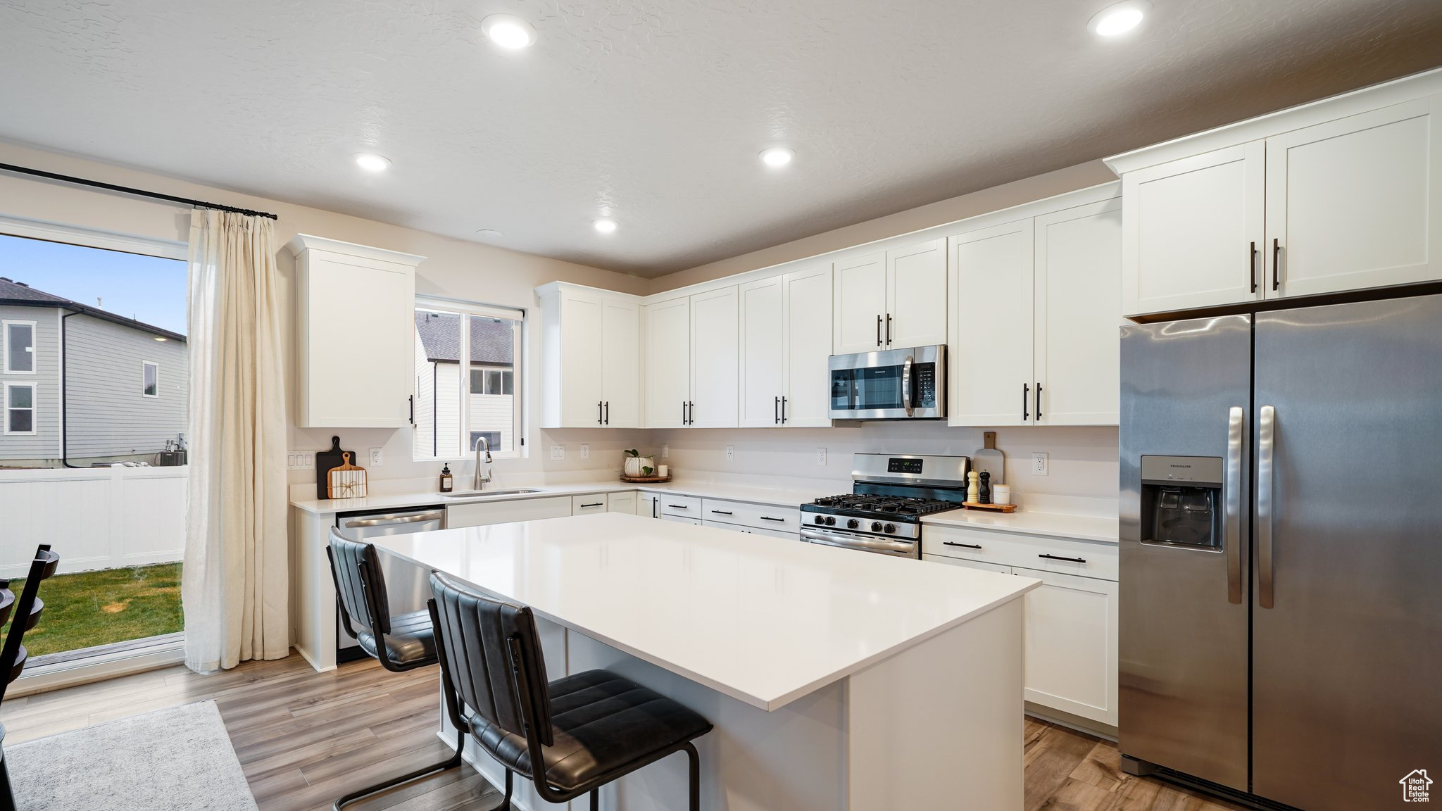 Kitchen with light hardwood / wood-style floors, a center island, white cabinetry, and stainless steel appliances