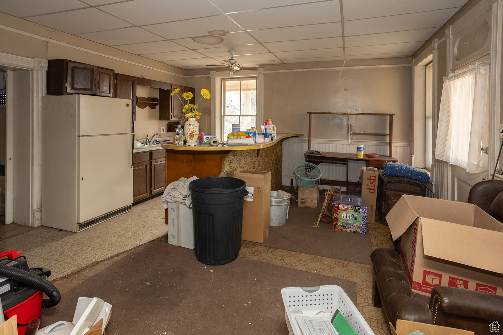 Basement with a paneled ceiling, ceiling fan, white refrigerator, and sink