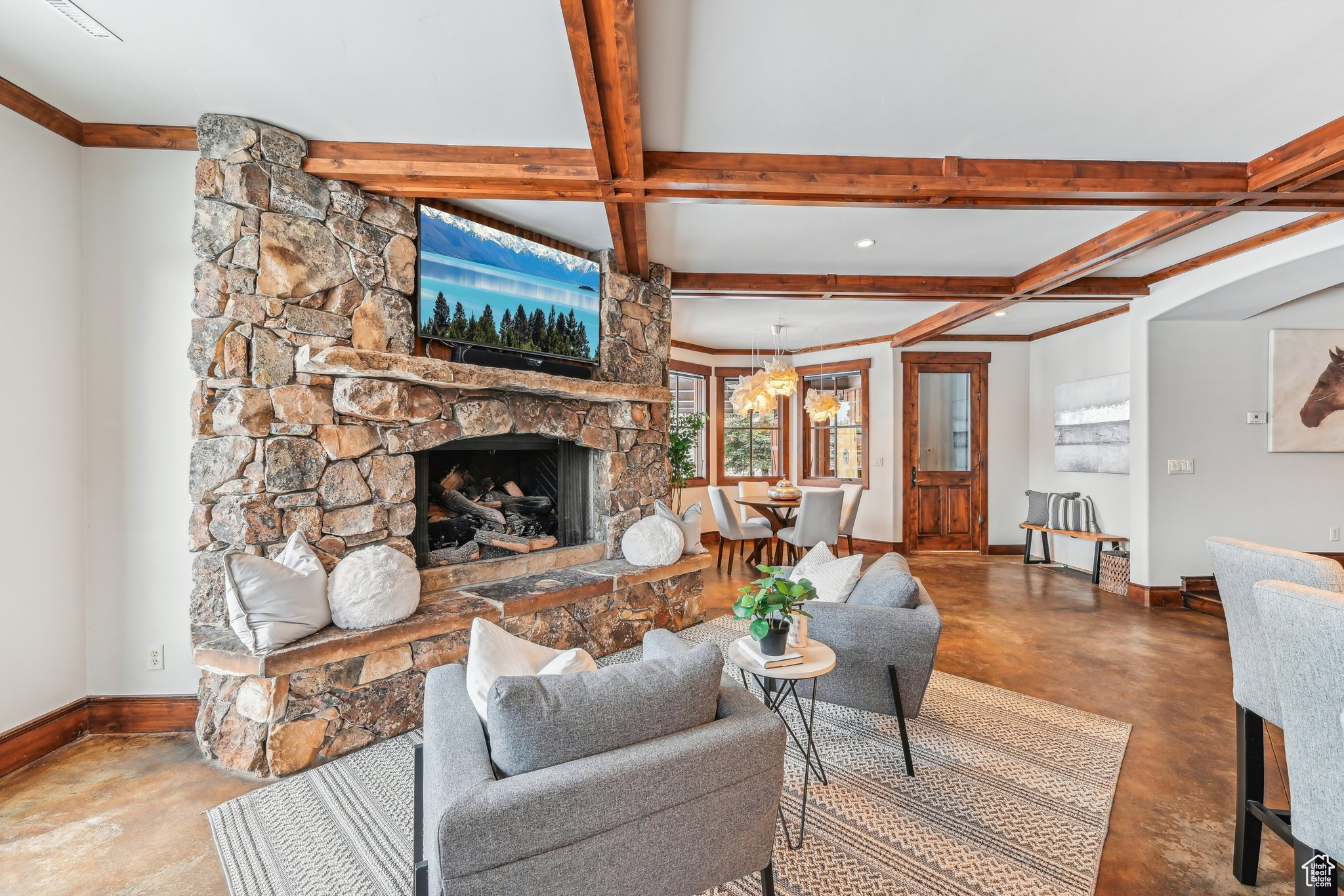 Living room featuring beam ceiling, coffered ceiling, a stone fireplace, a notable chandelier, and concrete floors