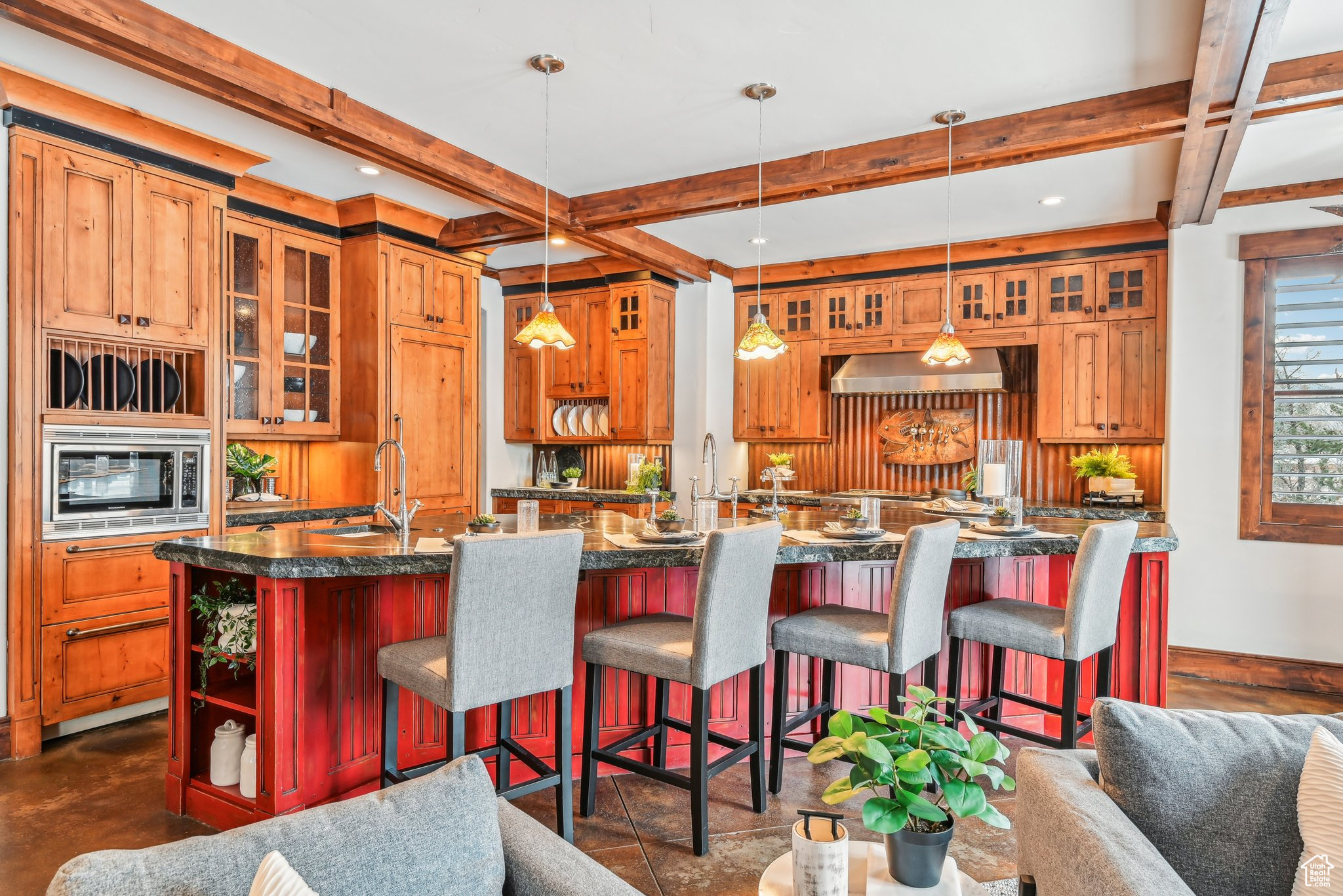 Kitchen featuring stainless steel microwave, sink, hanging light fixtures, dark stone counters, and a center island with sink