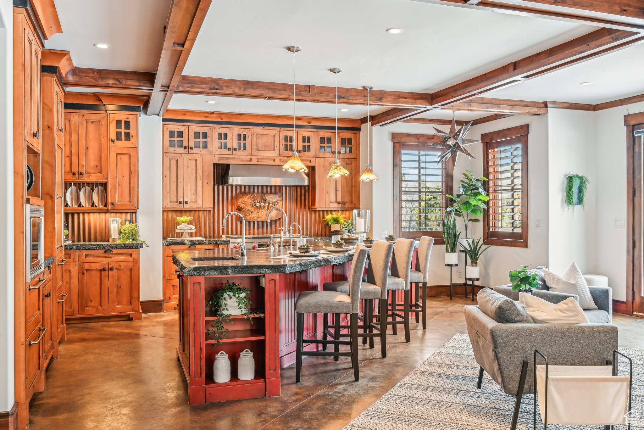 Kitchen featuring pendant lighting, a breakfast bar, a center island with sink, dark stone countertops, and beam ceiling