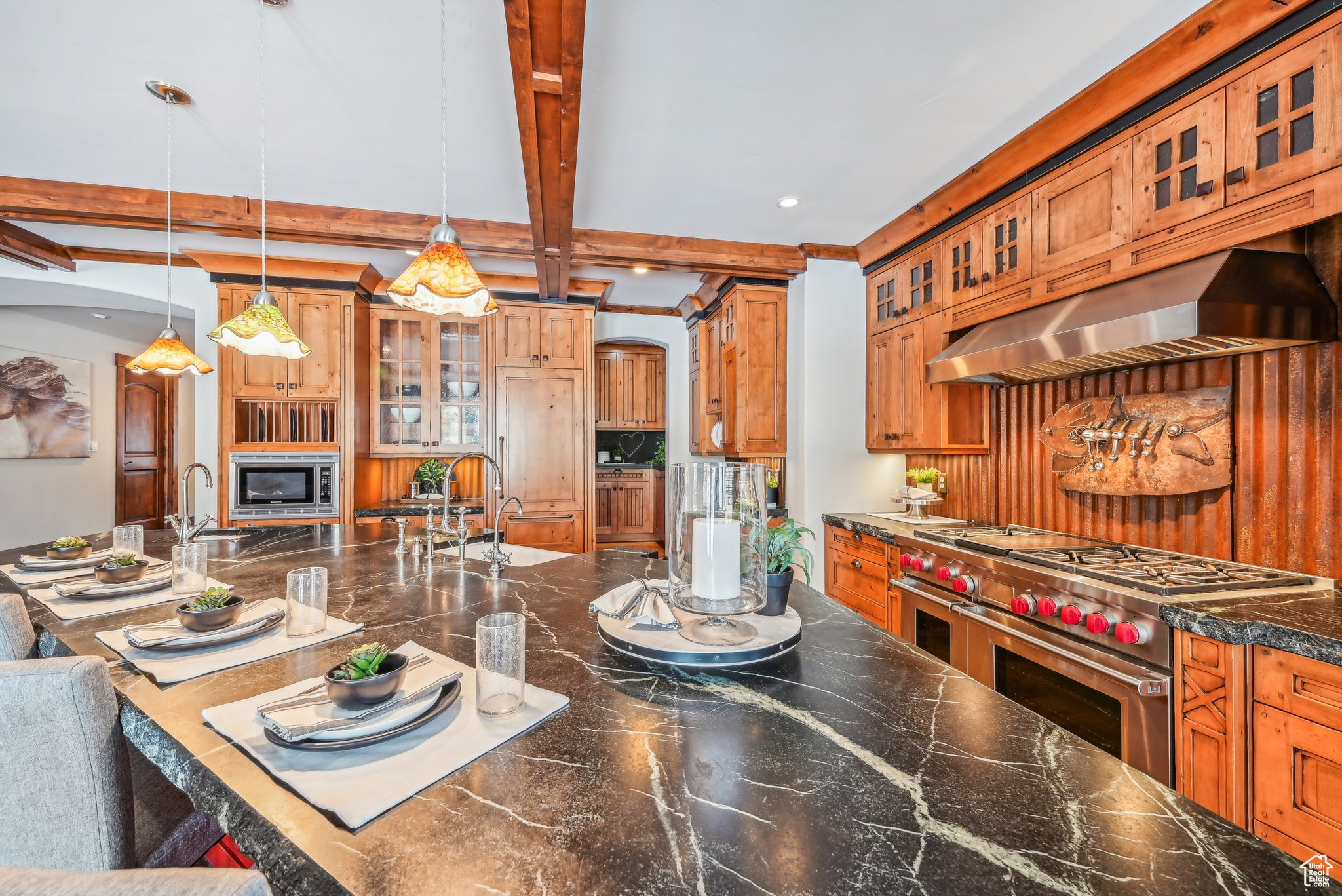 Kitchen with hanging light fixtures, wall chimney exhaust hood, beamed ceiling, a kitchen bar, and stainless steel appliances