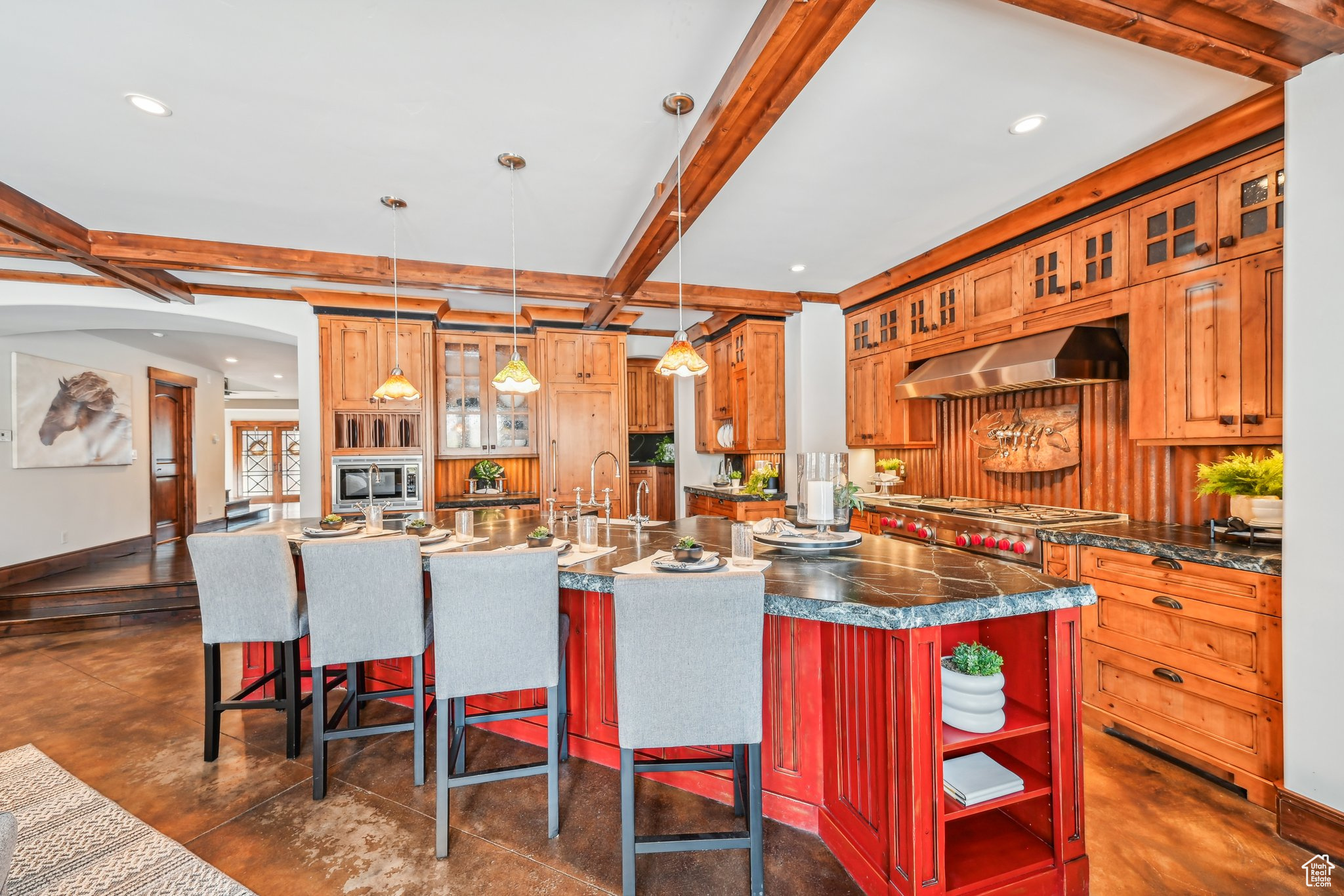 Kitchen with hanging light fixtures, beamed ceiling, ventilation hood, a center island with sink, and appliances with stainless steel finishes