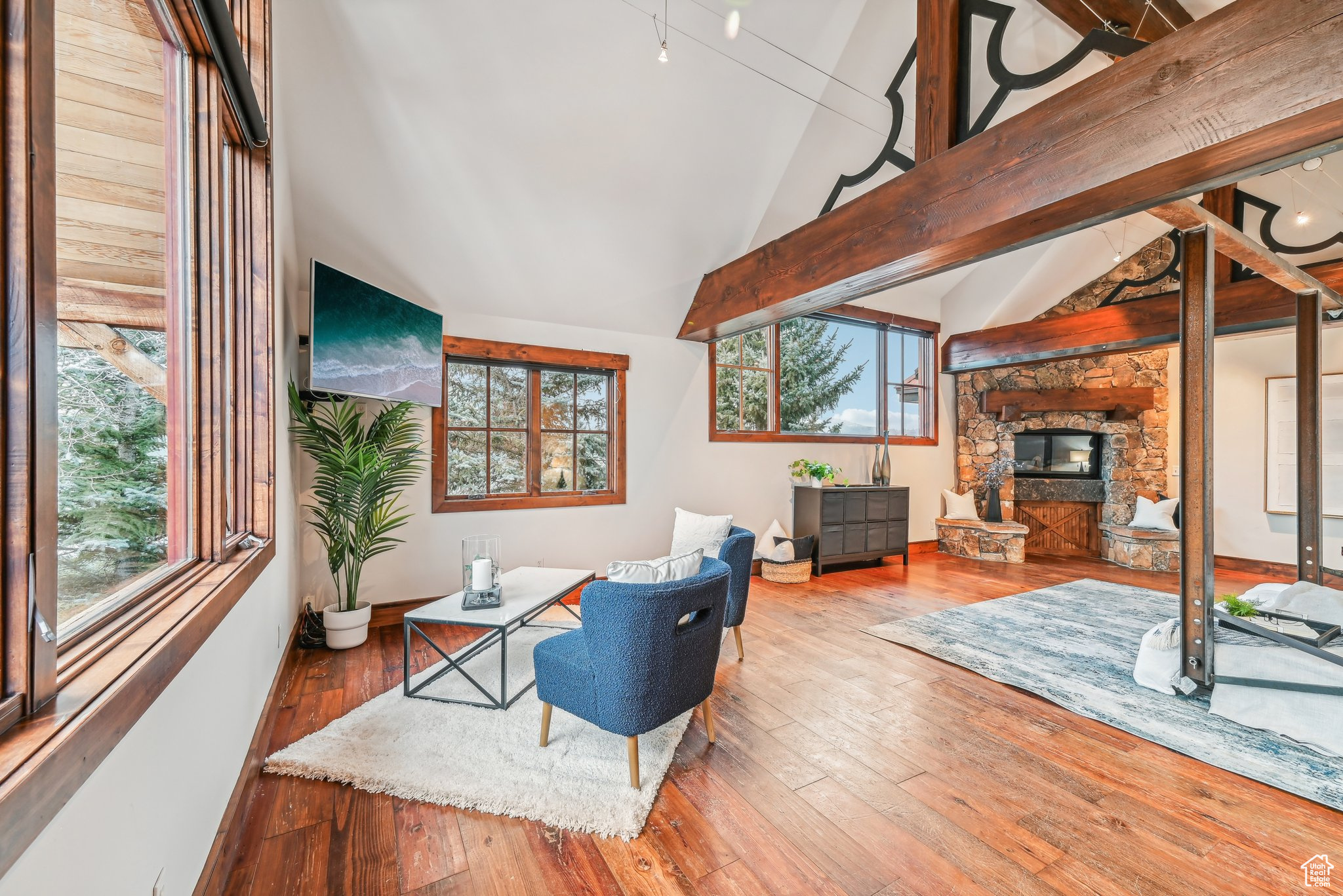 Living room with hardwood / wood-style floors, a stone fireplace, plenty of natural light, and lofted ceiling with beams