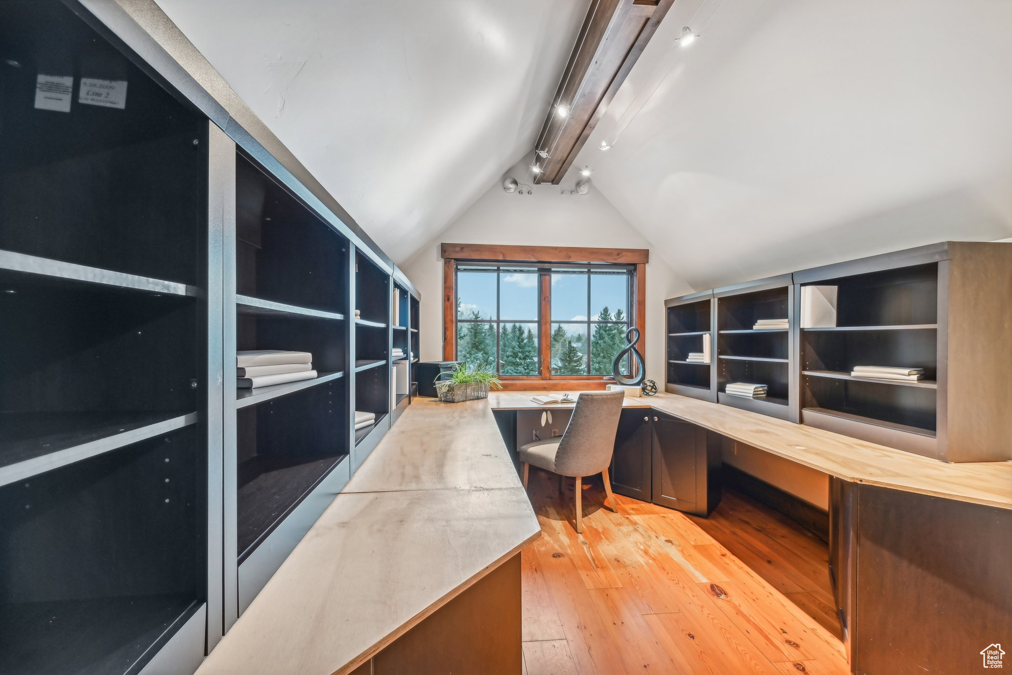 Office space with vaulted ceiling, light hardwood / wood-style flooring, built in desk, and track lighting