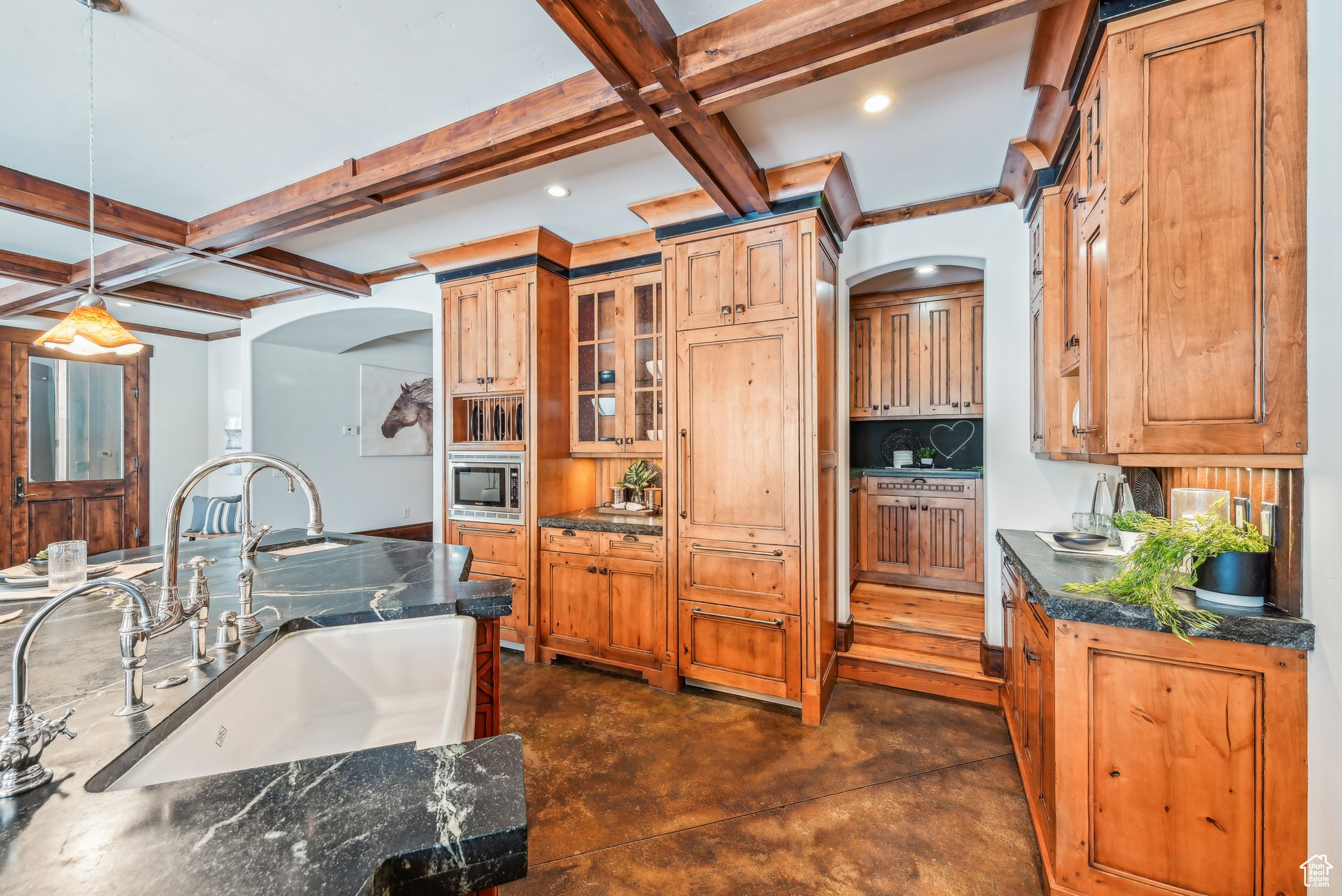 Kitchen featuring stainless steel microwave, coffered ceiling, sink, hanging light fixtures, and beam ceiling