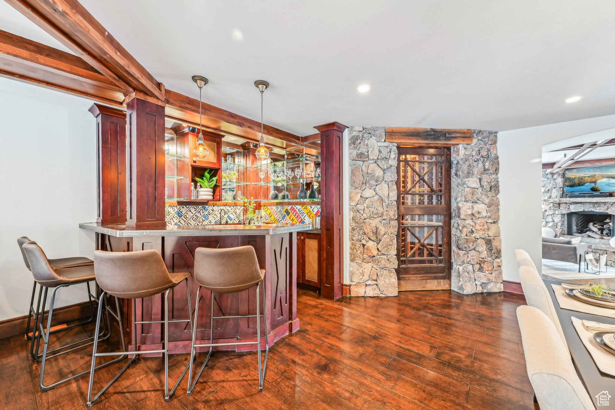 Bar featuring pendant lighting, a stone fireplace, dark hardwood / wood-style floors, ornate columns, and tasteful backsplash