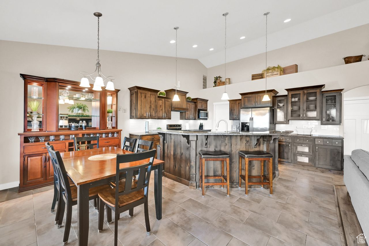 Tiled dining area with sink, high vaulted ceiling, and beautiful lighting.