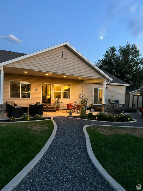 Back of house with a lawn, an outdoor living space, a patio area, and a shed