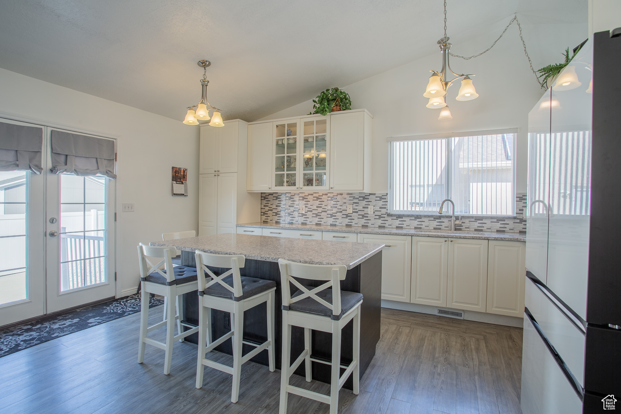 Kitchen featuring white cabinetry, an inviting chandelier, vaulted ceiling, decorative backsplash, and a kitchen island