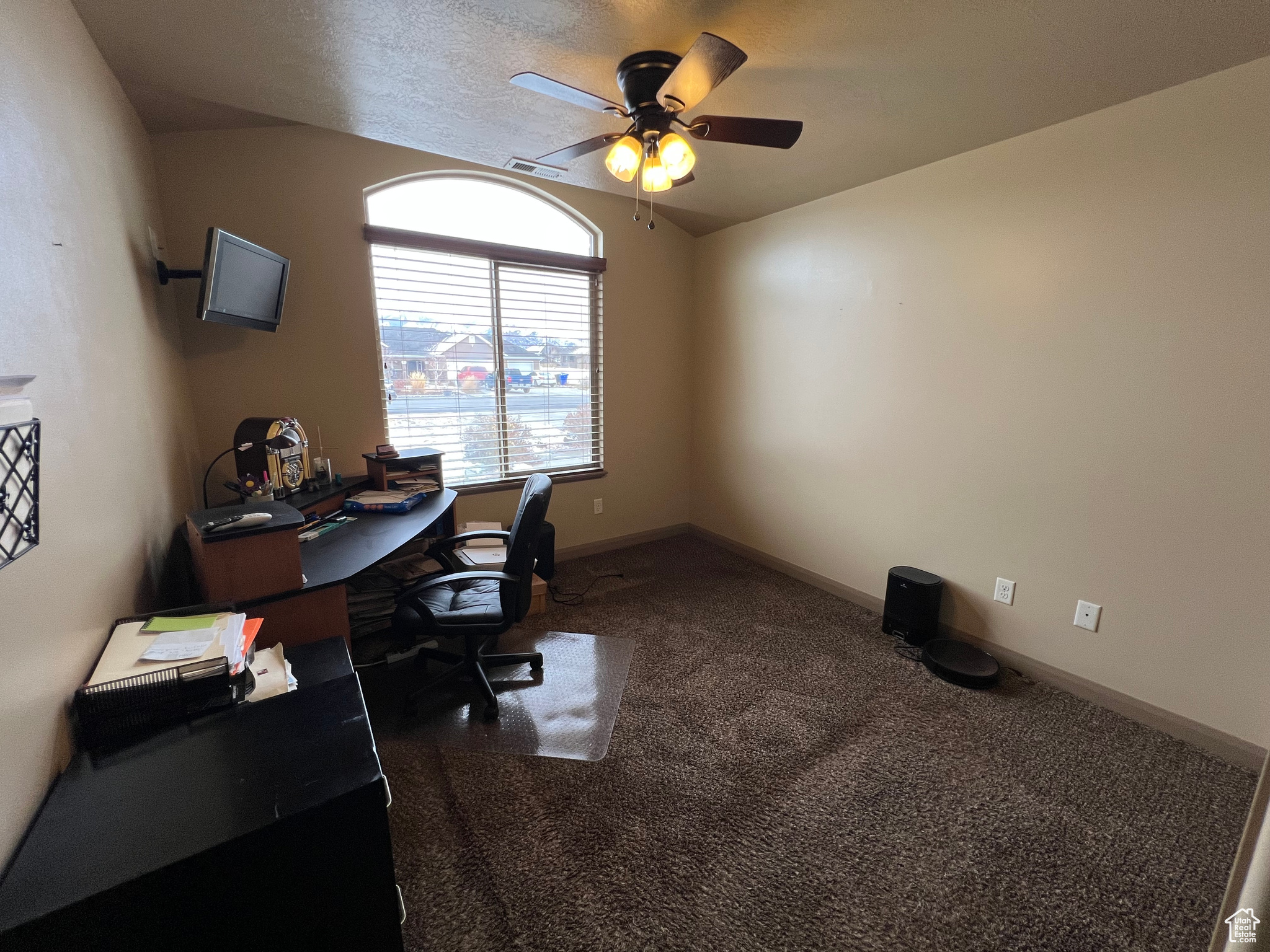 Carpeted home office featuring a textured ceiling, vaulted ceiling, and ceiling fan