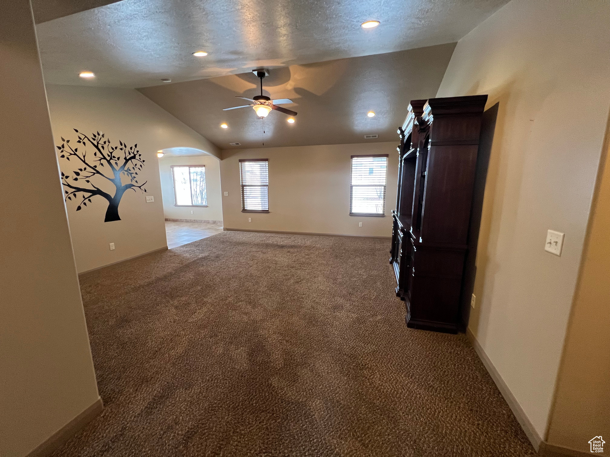 Unfurnished living room featuring carpet flooring, ceiling fan, a textured ceiling, and vaulted ceiling