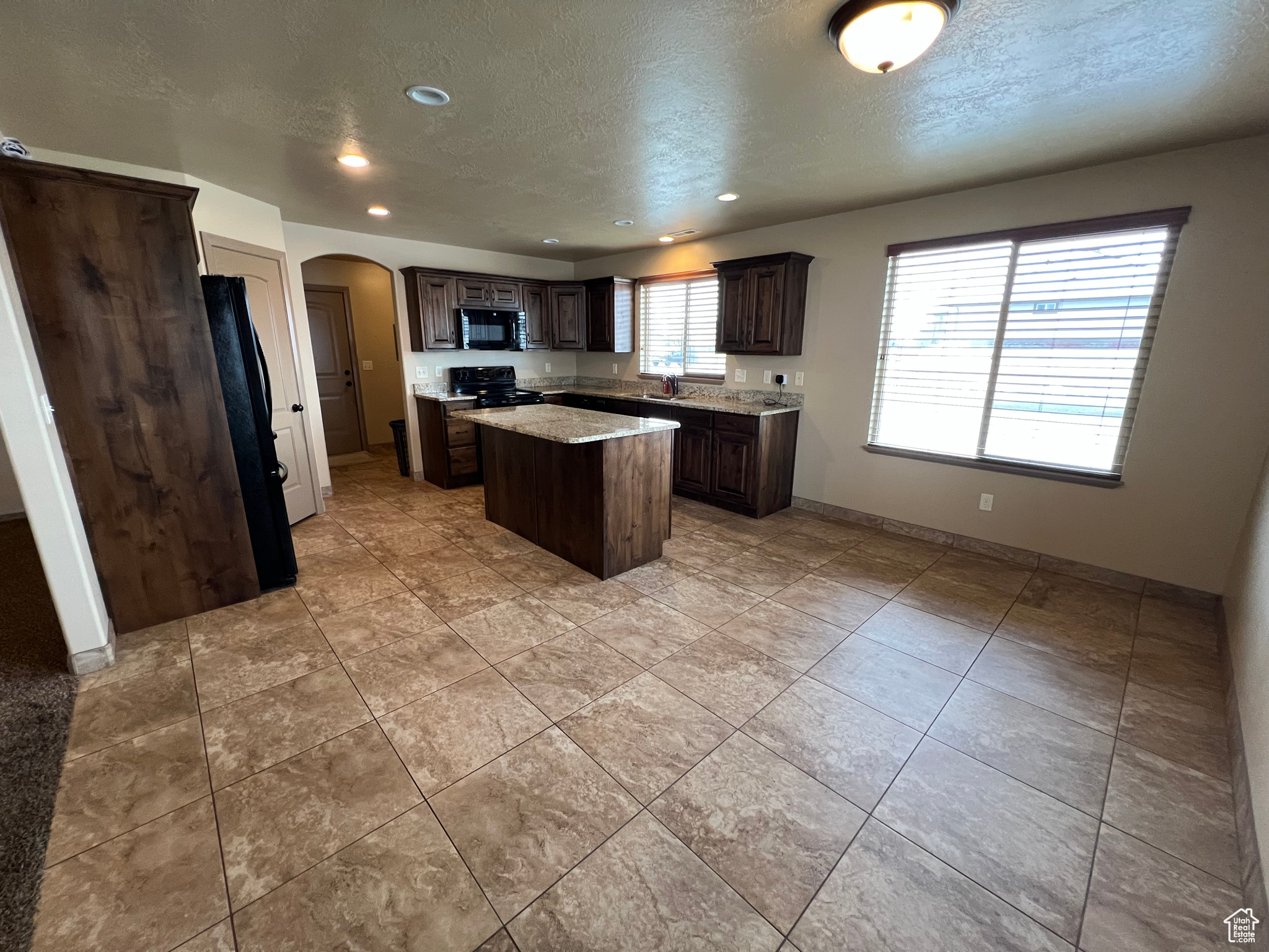 Kitchen with black appliances, light tile patterned floors, a textured ceiling, dark brown cabinets, and a kitchen island