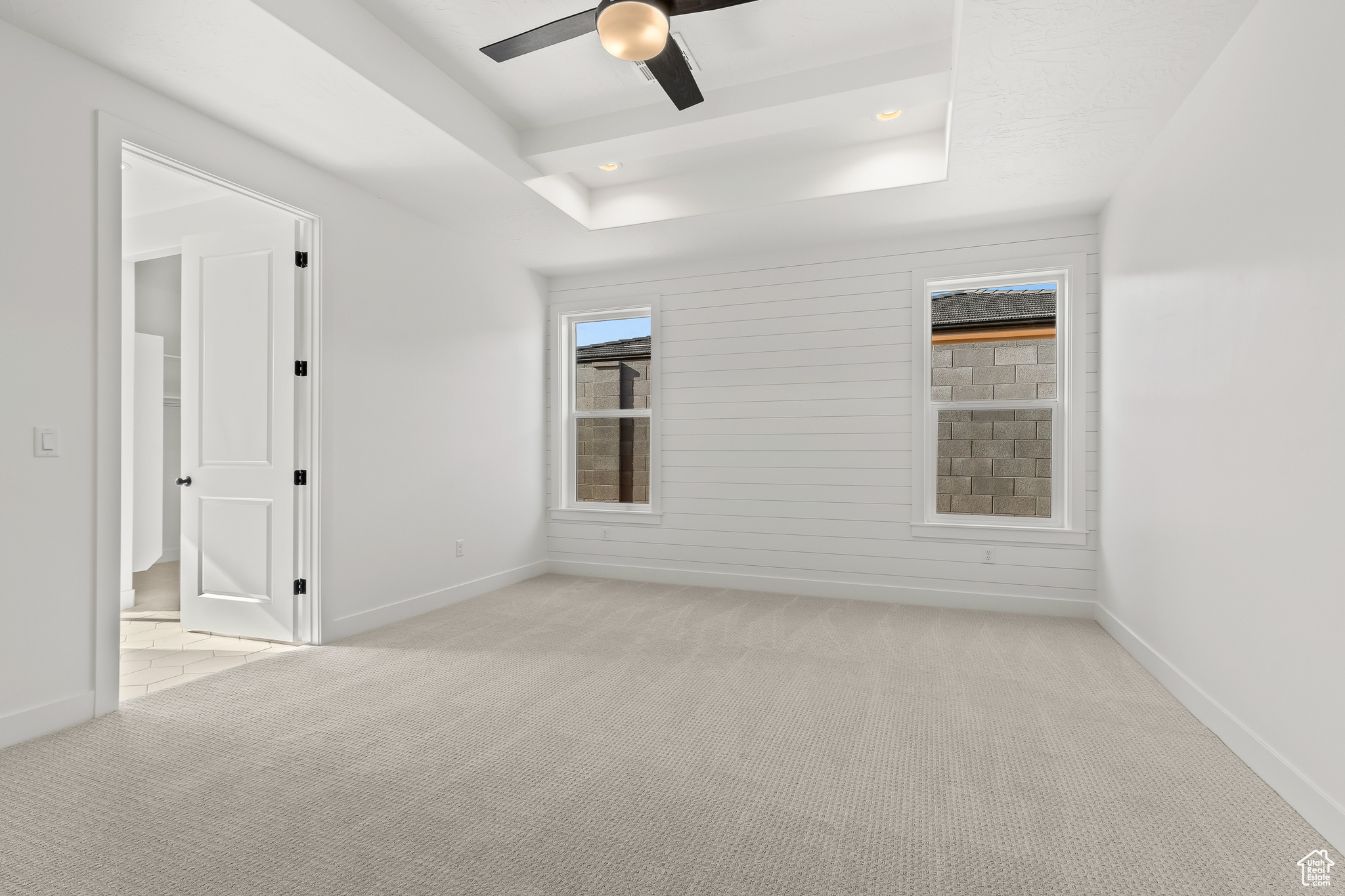 Carpeted empty room featuring a raised ceiling, ceiling fan, and wooden walls