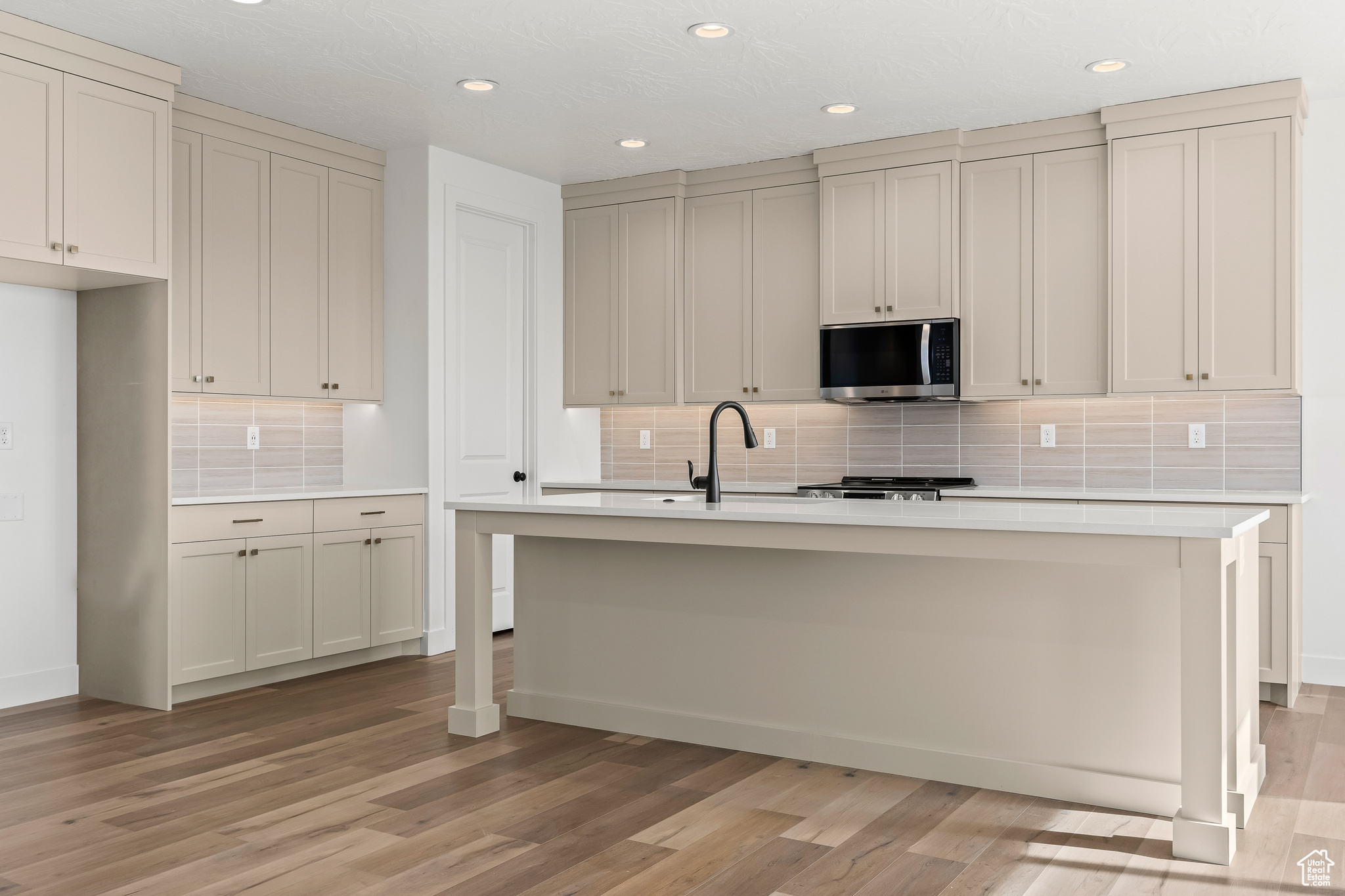 Kitchen with decorative backsplash, light hardwood / wood-style flooring, a kitchen island with sink, and sink