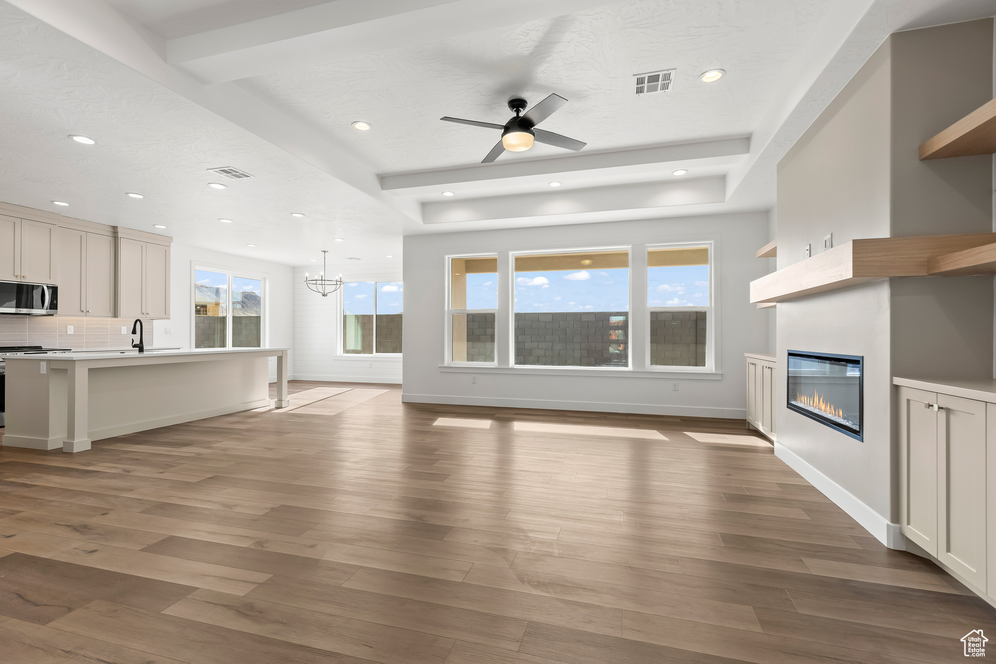 Unfurnished living room featuring sink, ceiling fan with notable chandelier, and light wood-type flooring