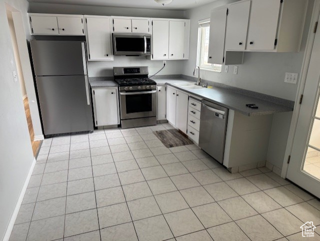 Kitchen featuring white cabinets, light tile patterned floors, sink, and appliances with stainless steel finishes