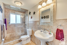 Bathroom featuring a tile shower, sink, tile walls, tile patterned flooring, and toilet