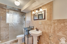 Bathroom featuring a textured ceiling, tile walls, and toilet