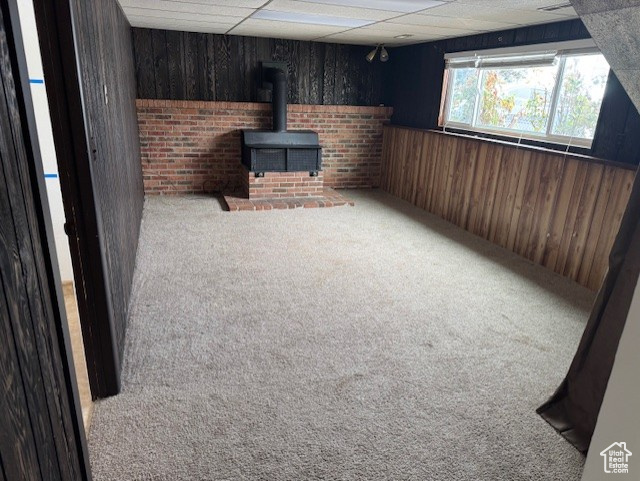 Basement featuring carpet flooring, a wood stove, and wooden walls