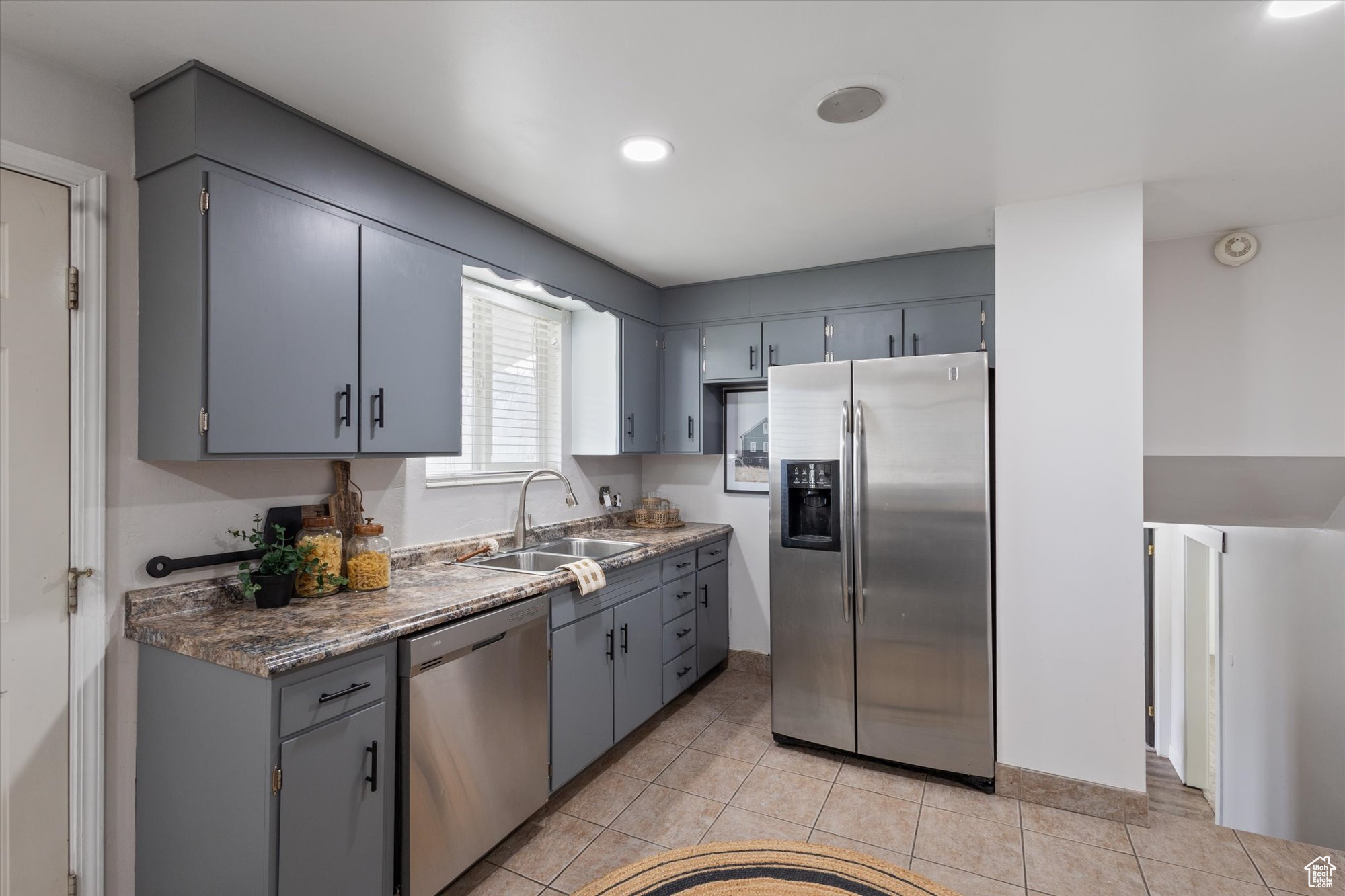 Kitchen with gray cabinetry, light tile patterned floors, sink, and appliances with stainless steel finishes