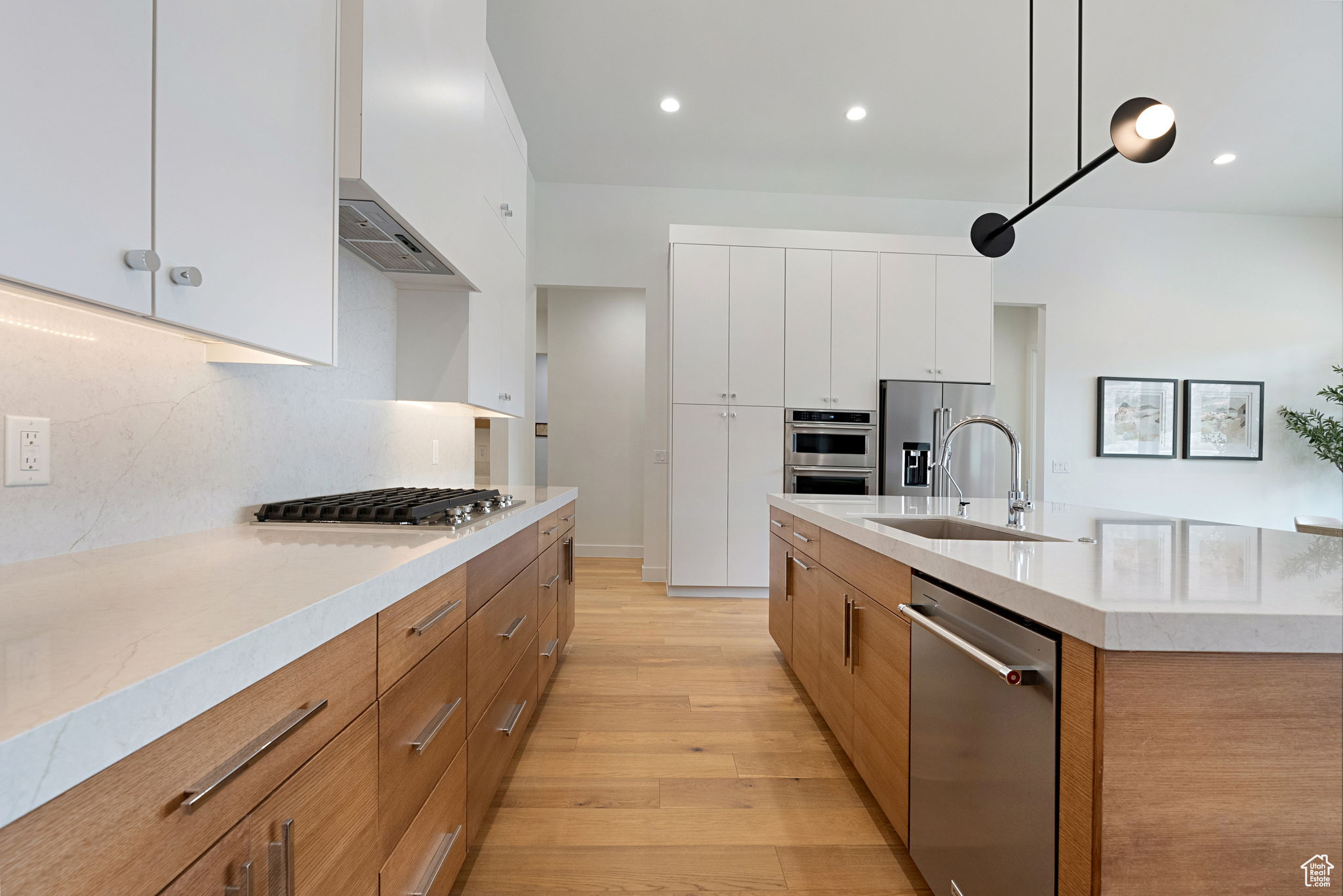 Kitchen with white cabinetry, sink, hanging light fixtures, stainless steel appliances, and a center island with sink