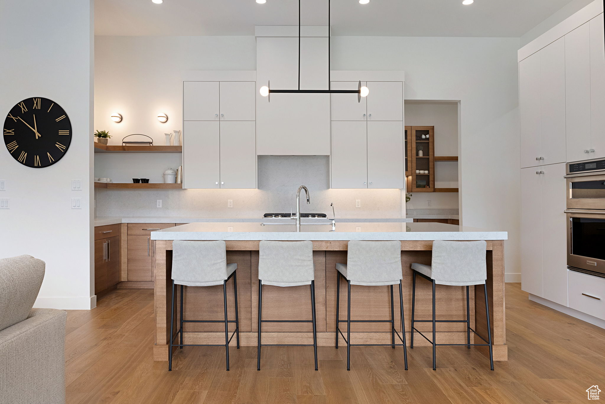 Kitchen with white cabinets, a center island with sink, double oven, and light hardwood / wood-style flooring