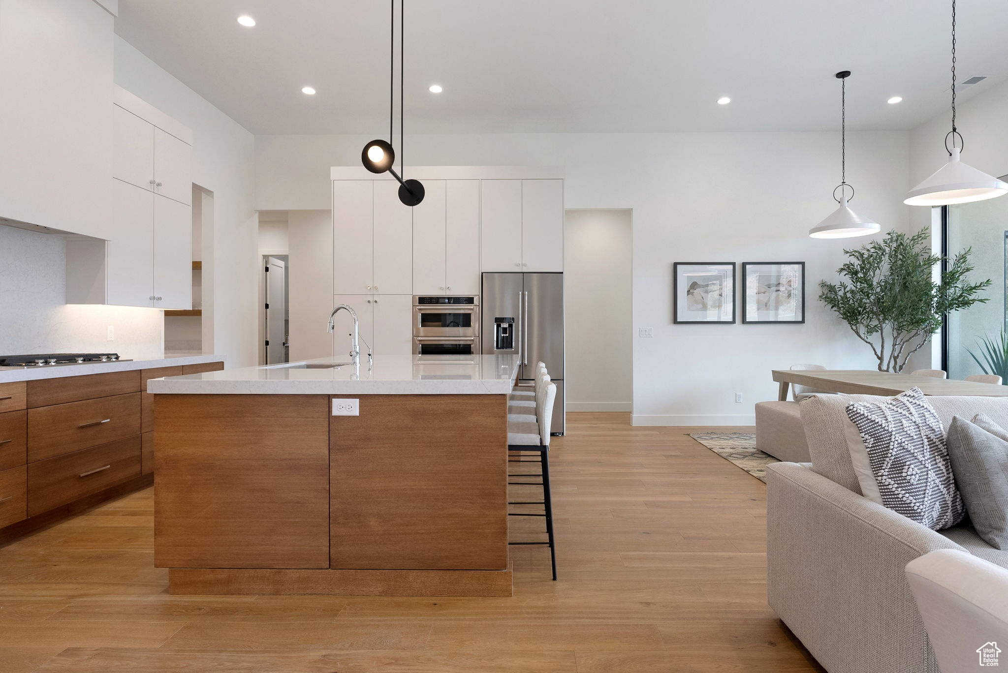 Kitchen with hanging light fixtures, light hardwood / wood-style flooring, an island with sink, white cabinetry, and stainless steel appliances